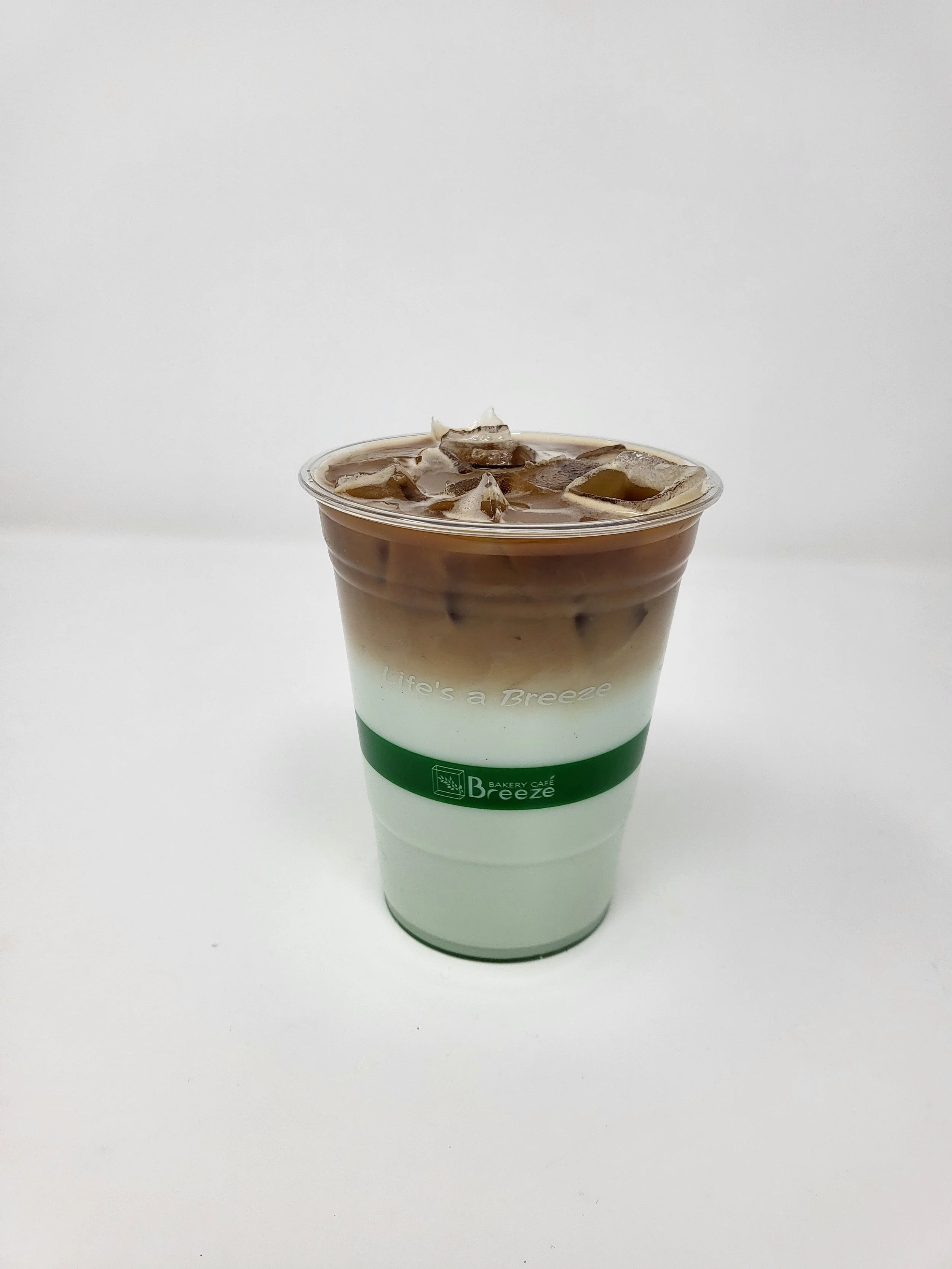 Iced pandan latte in clear plastic cup, espresso at the top is slowly mixing with the light green colored pandan milk from the lower half of the cup.