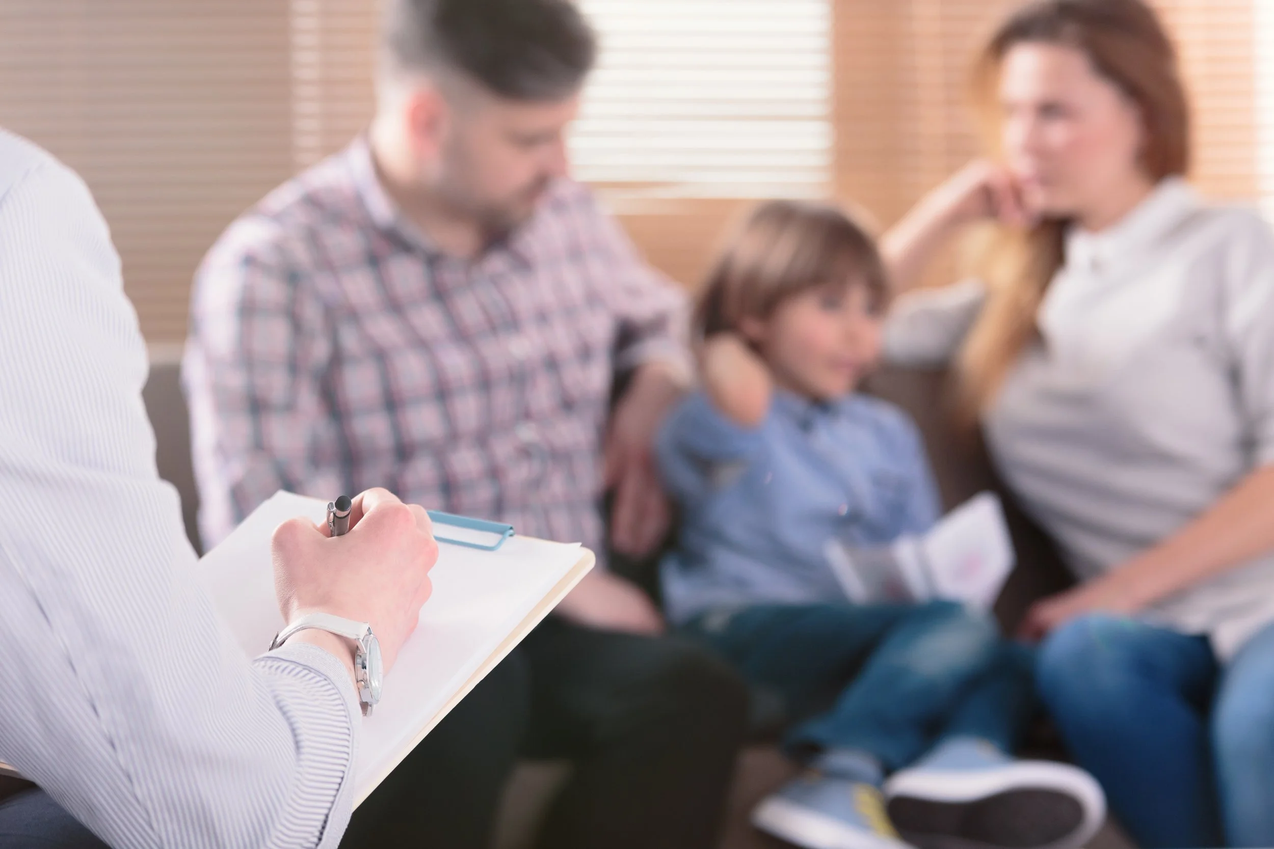 A group of people attending a meeting, with focused individuals taking notes and listening attentively.
