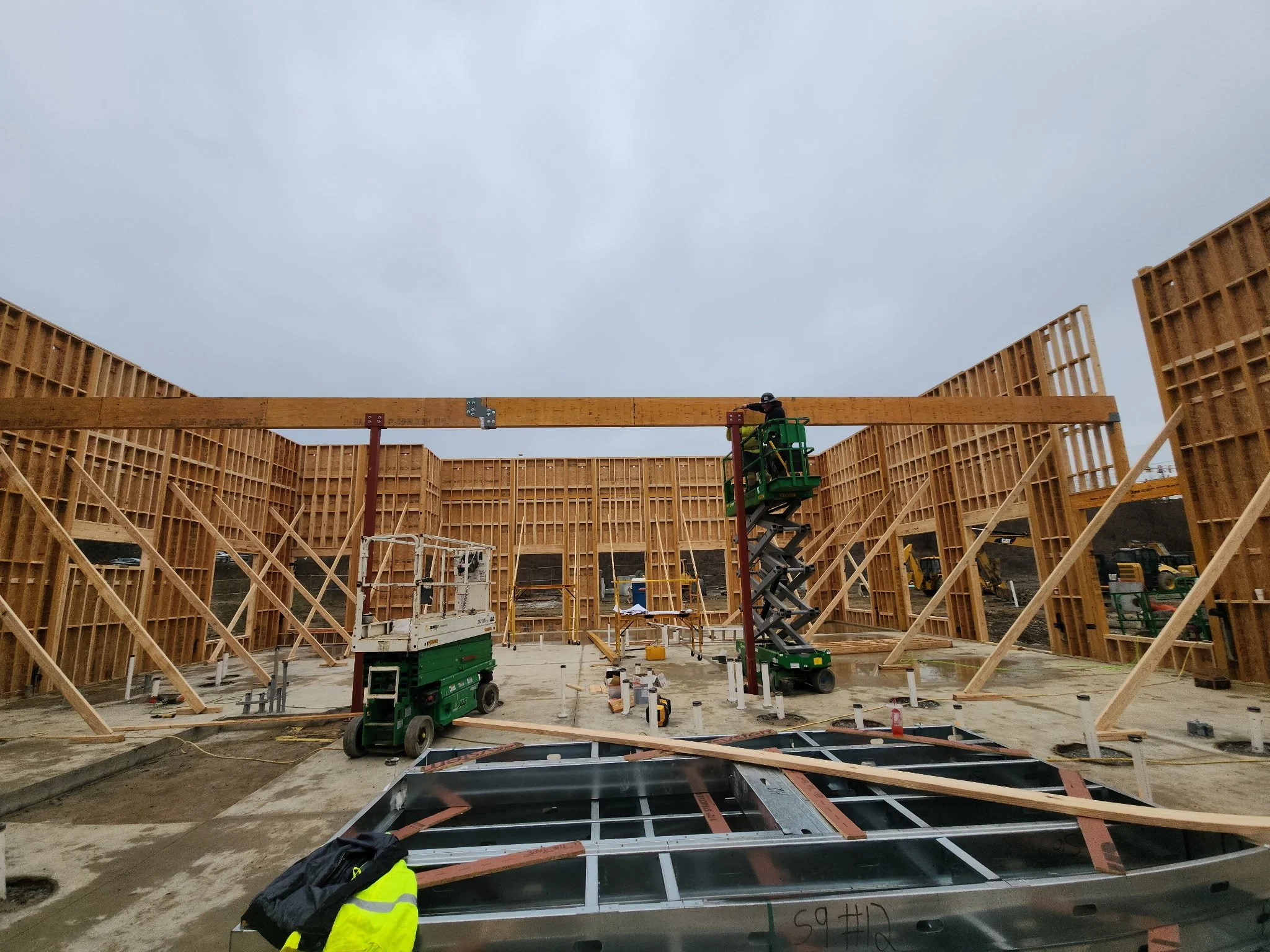 Construction site with wooden framing, scaffolding, and construction equipment under a cloudy sky.