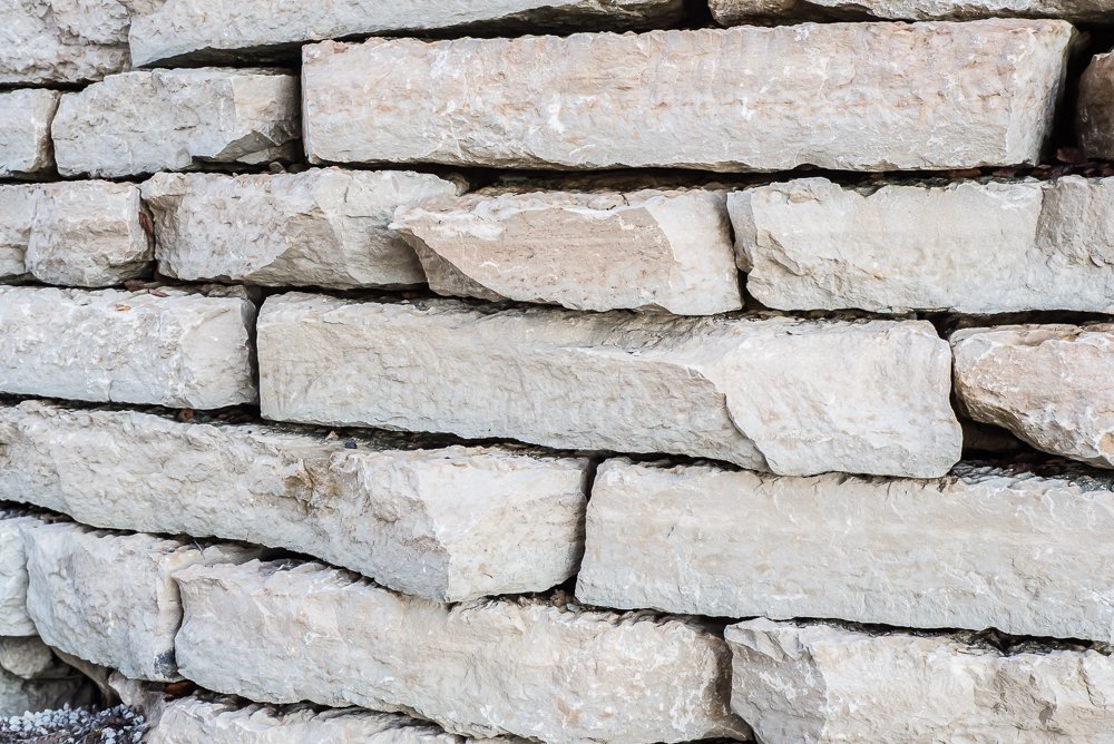 Close-up of a stacked stone wall with irregularly shaped, light-colored stones.