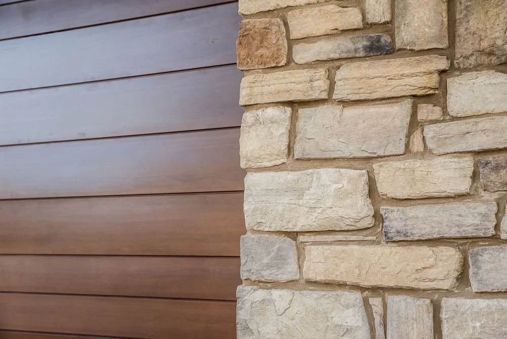 Close-up of a wall showing a transition from horizontal wooden siding to stacked stone veneer.