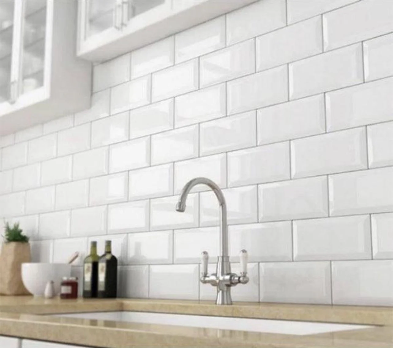 Kitchen with white subway tile backsplash, a silver faucet, a beige countertop, a potted plant, two bottles, a bowl, and small jars.