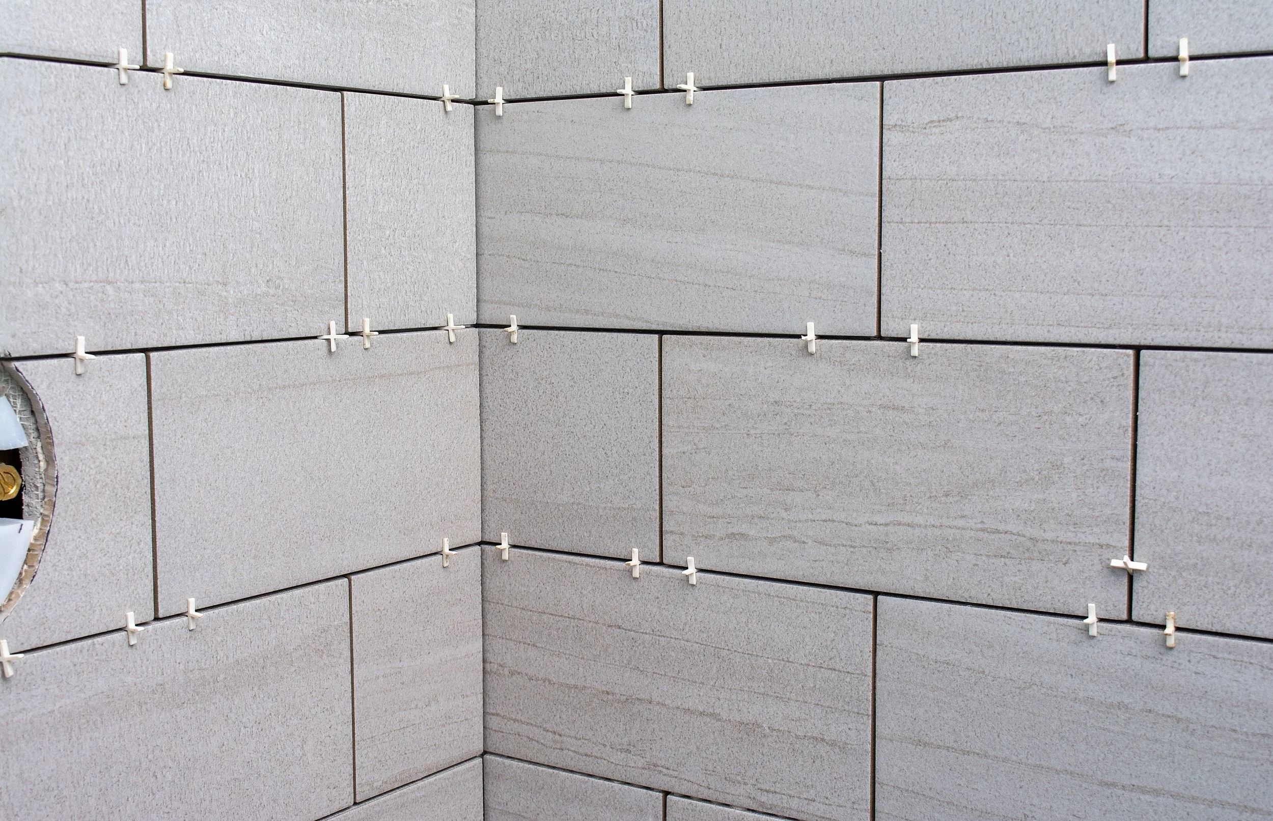 Close-up of tiled wall with tile spacers in place, showing the process of tiling and alignment.
