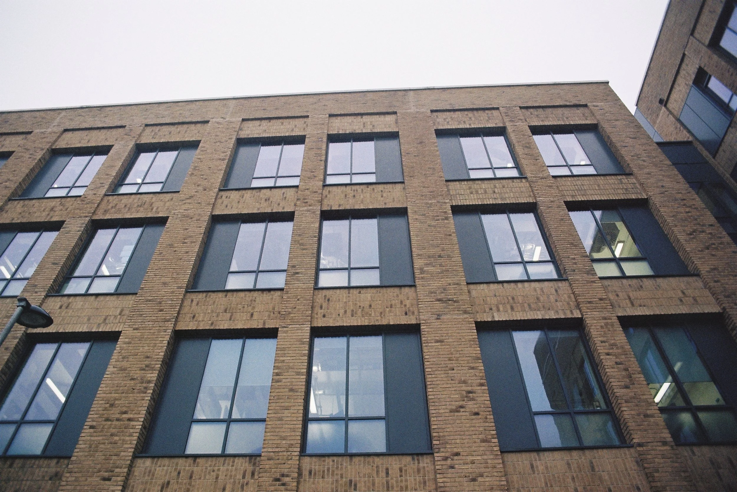 A tall brick building with multiple windows viewed from below, with a gray overcast sky in the background.
