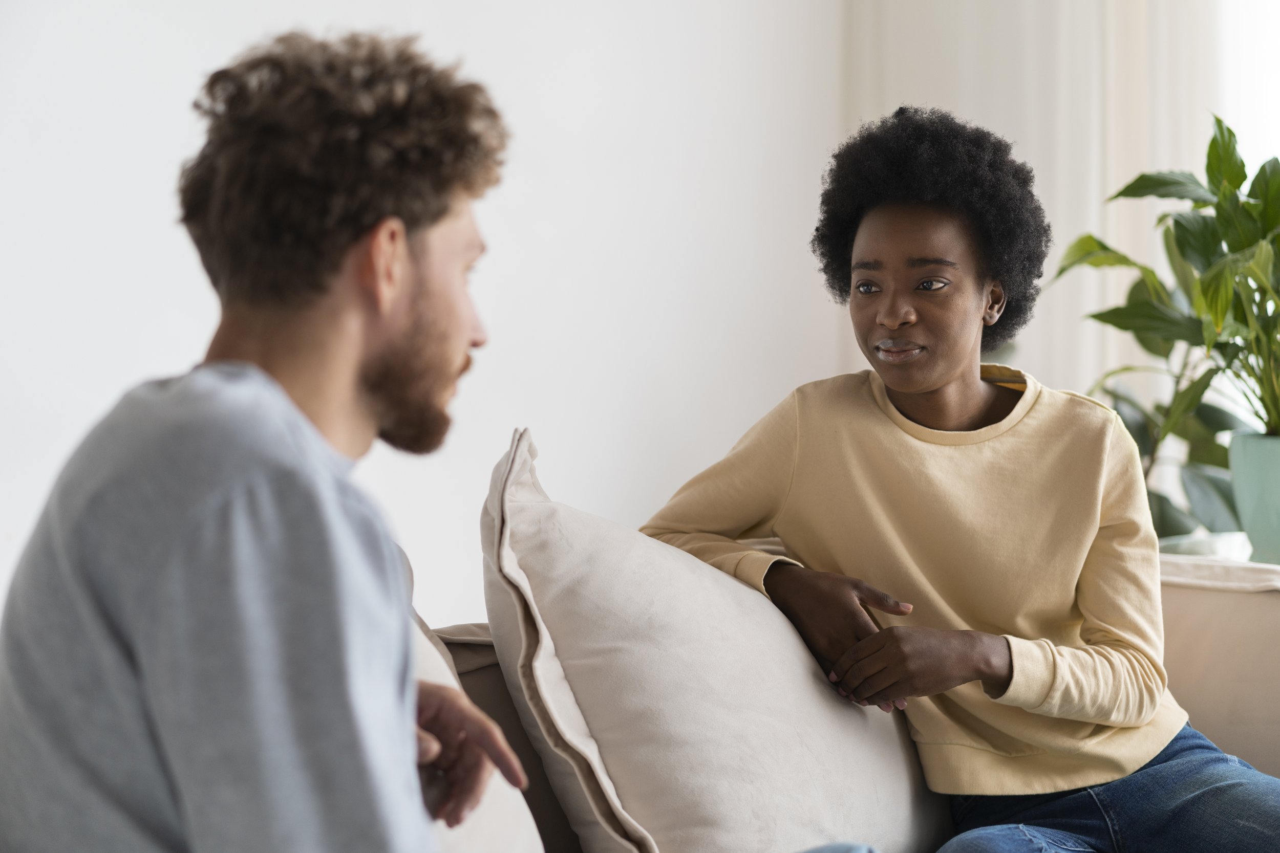 A woman and a man having a conversation on a sofa, with the woman appearing to be listening attentively.