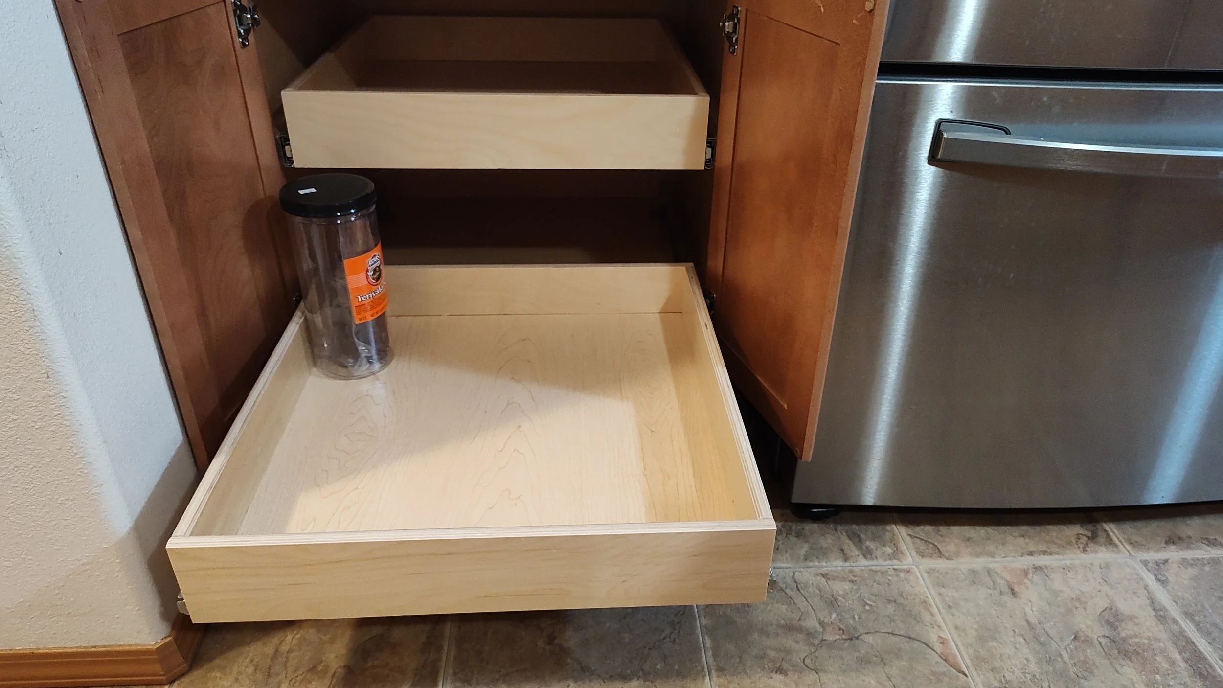 Empty kitchen cabinet drawer with a plastic container on the left and a partially opened drawer above.