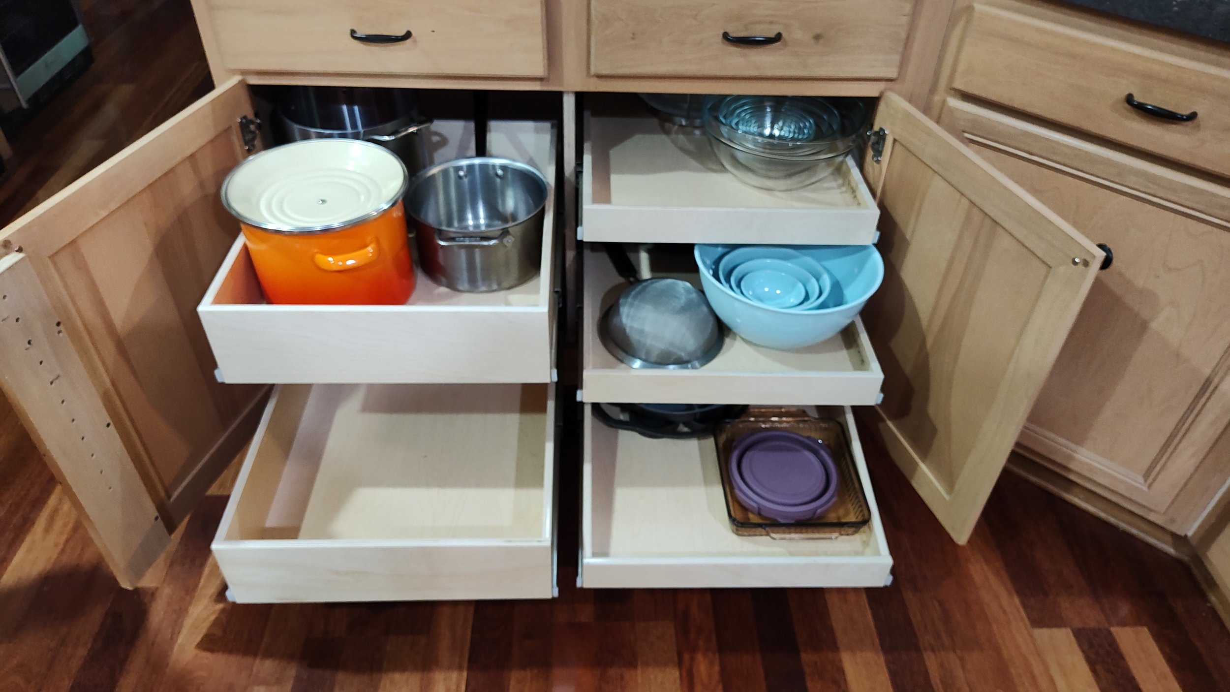 Open kitchen cabinet drawers containing colorful pots, plates, and bowls