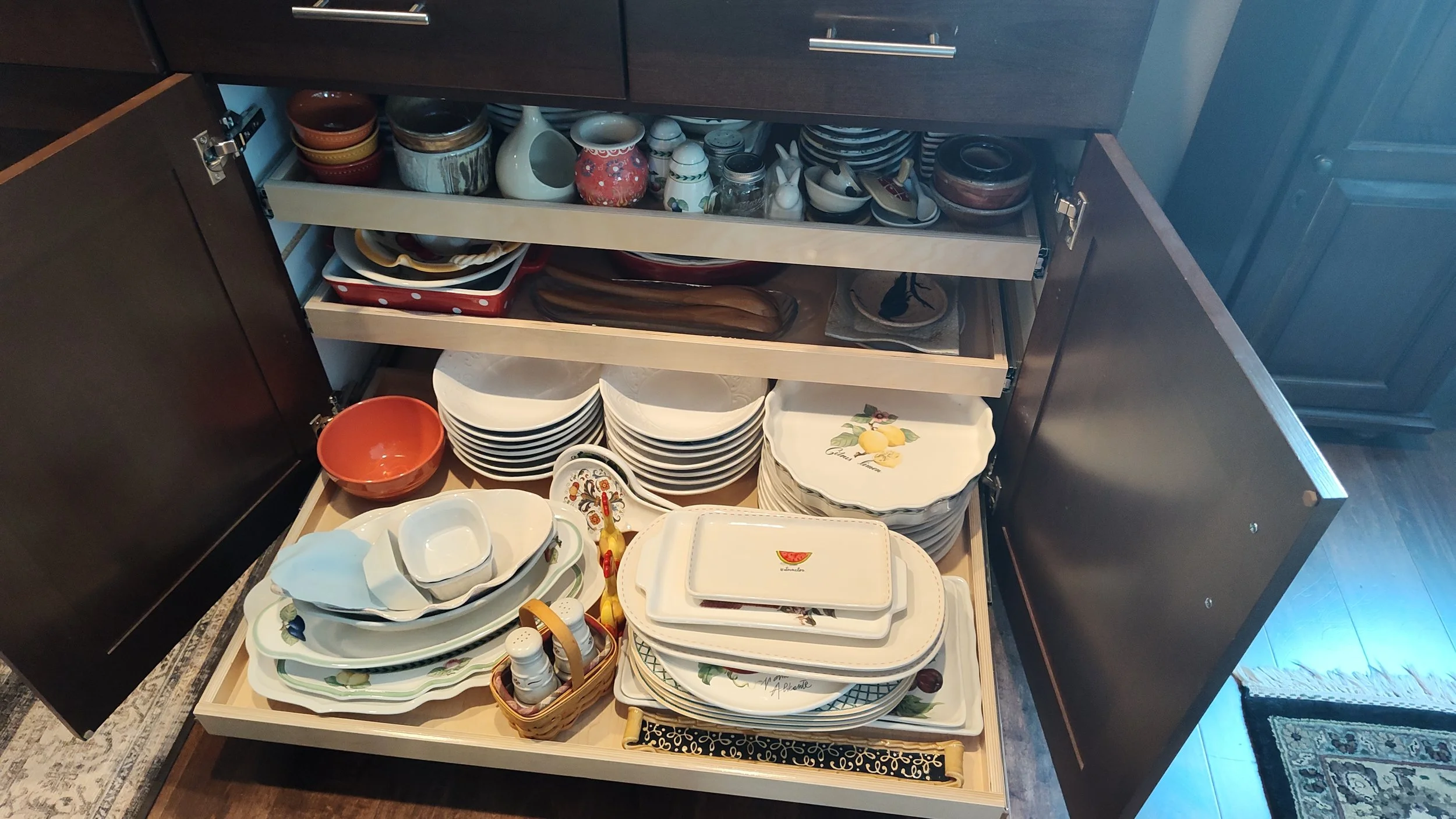 Open kitchen cabinet with dishes, bowls, plates, and cups neatly arranged on shelves and inside drawers.