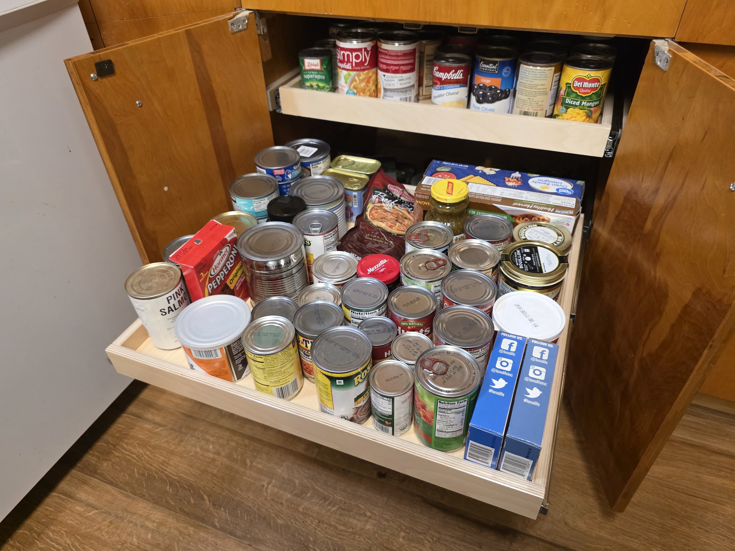 Open kitchen cabinet filled with canned foods, boxed food items, and jars.