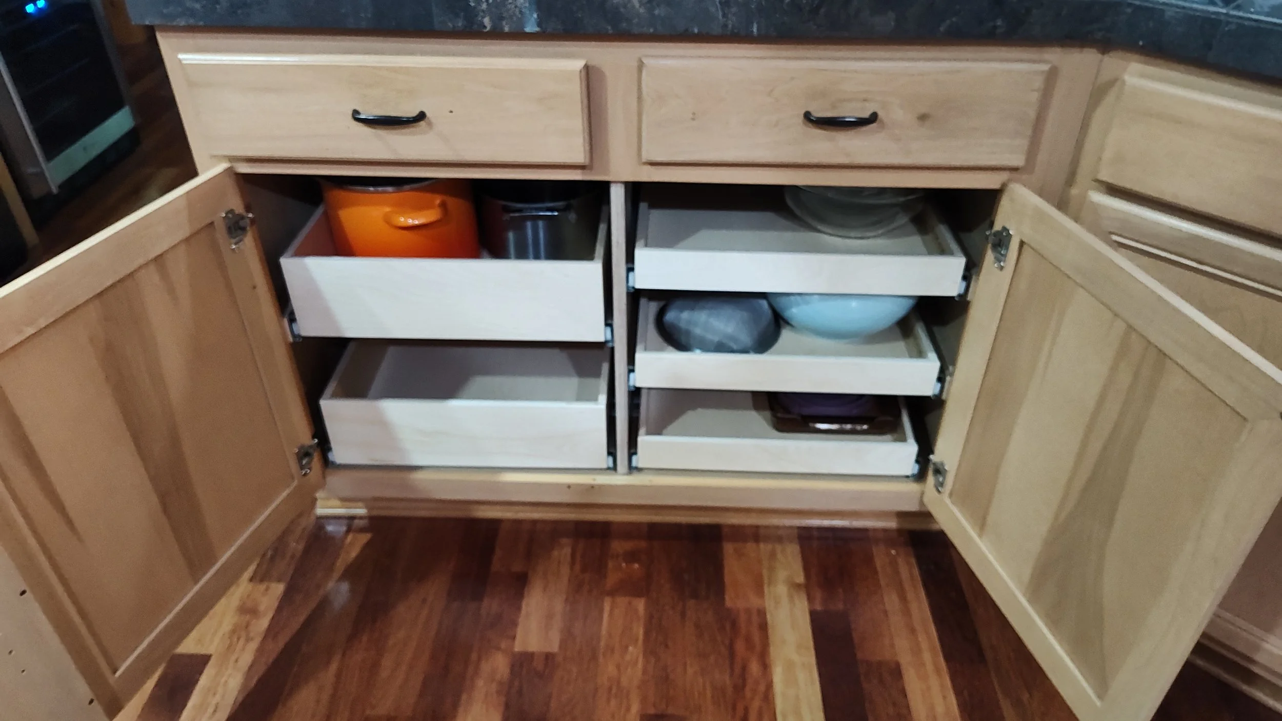 Open kitchen cabinet with multiple shelves and white drawers containing various bowls and containers.