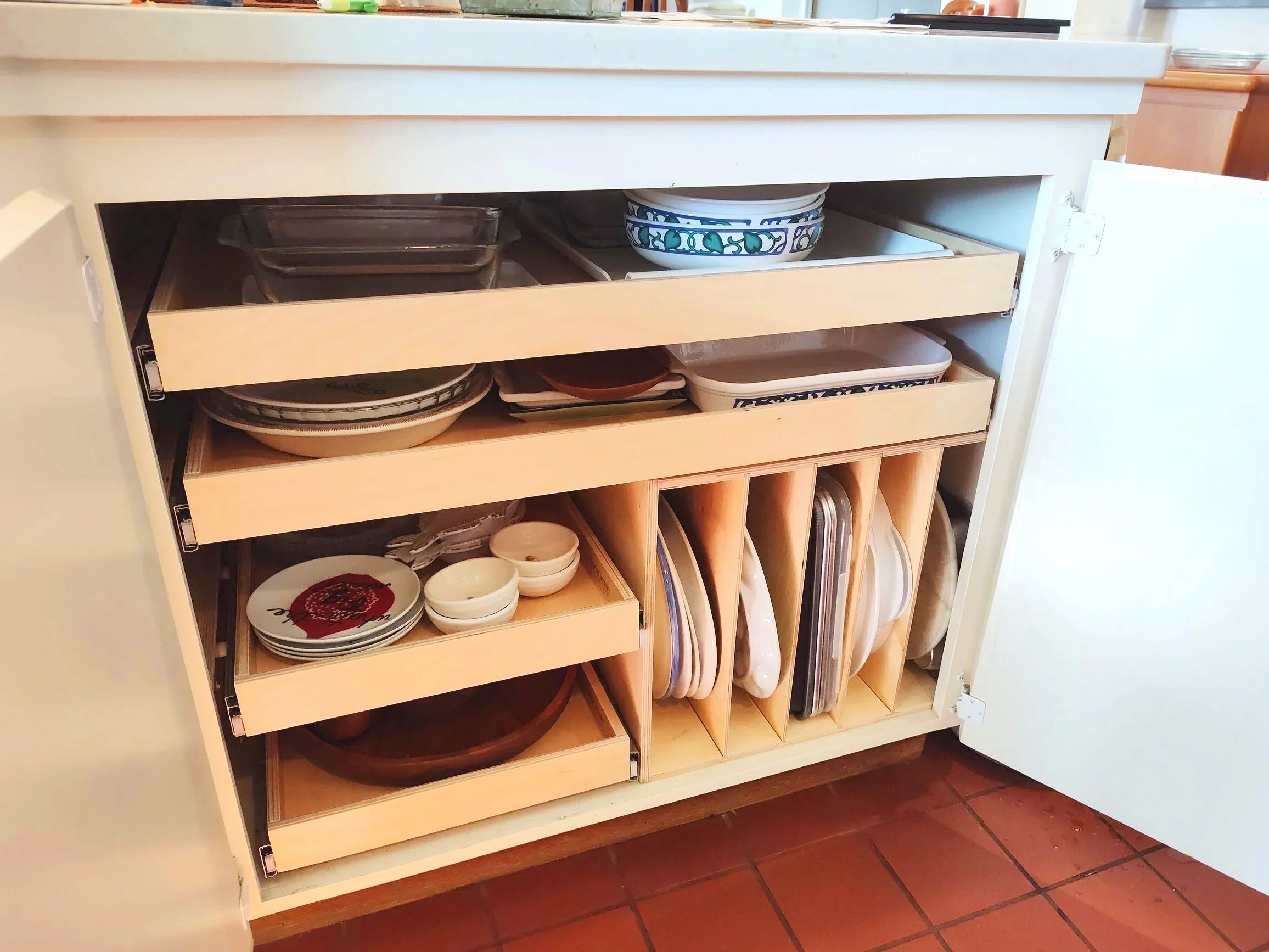 Open kitchen cabinet showing stacked dishes, bowls, and plates organized in wooden dividers and shelves.