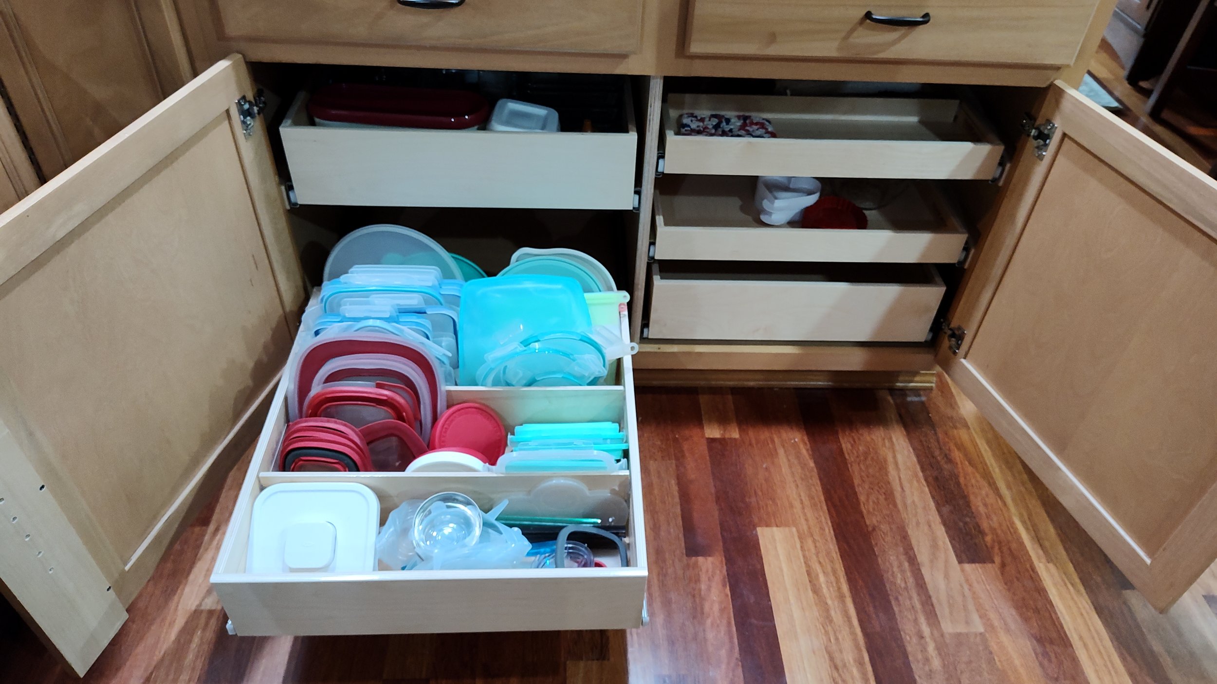 Open kitchen cabinet with plastic food storage containers in various colors and sizes in the drawer and inside the cabinet.