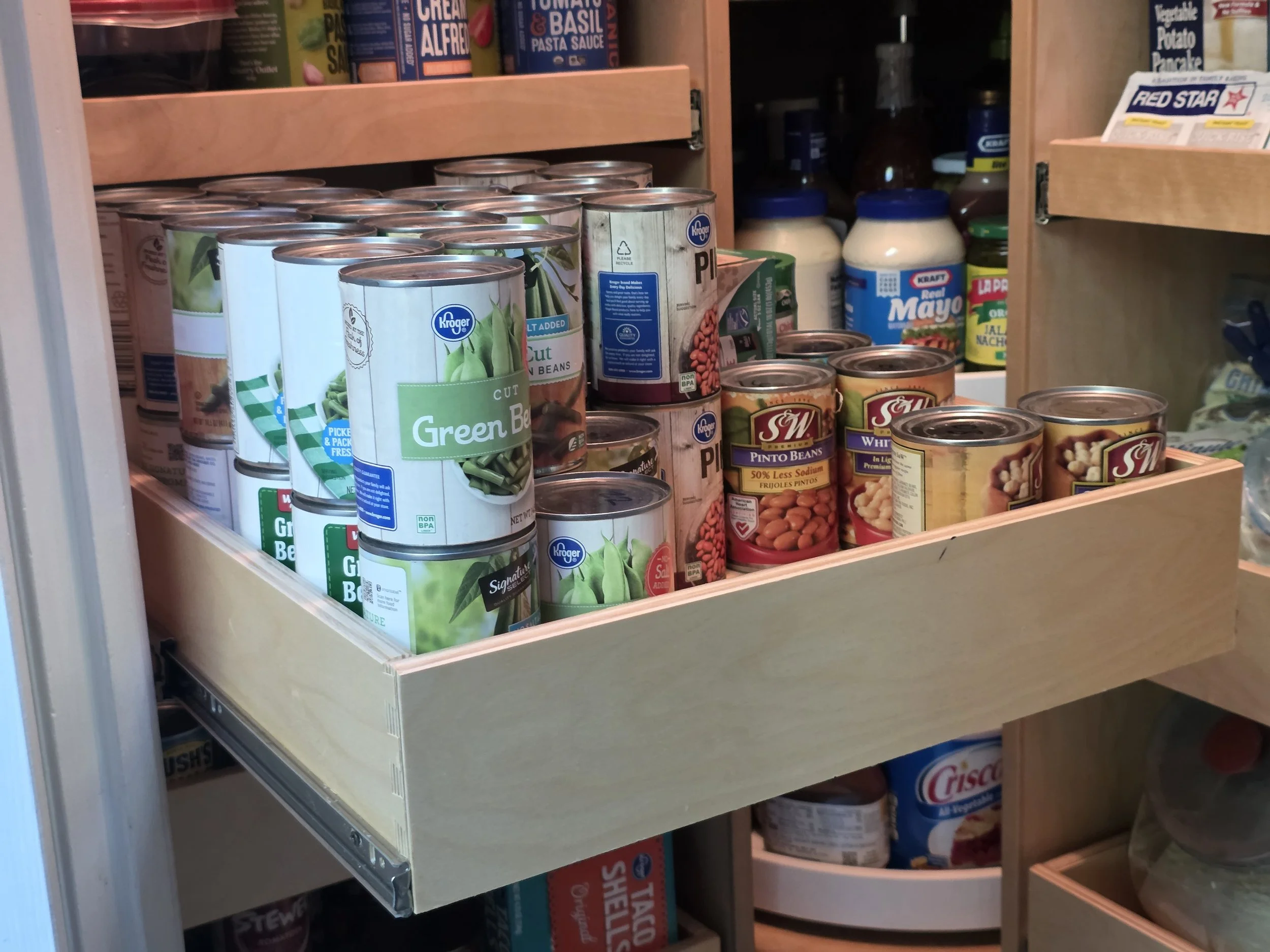 A wooden pantry drawer filled with canned vegetables, including green beans, pinto beans, and chickpeas.