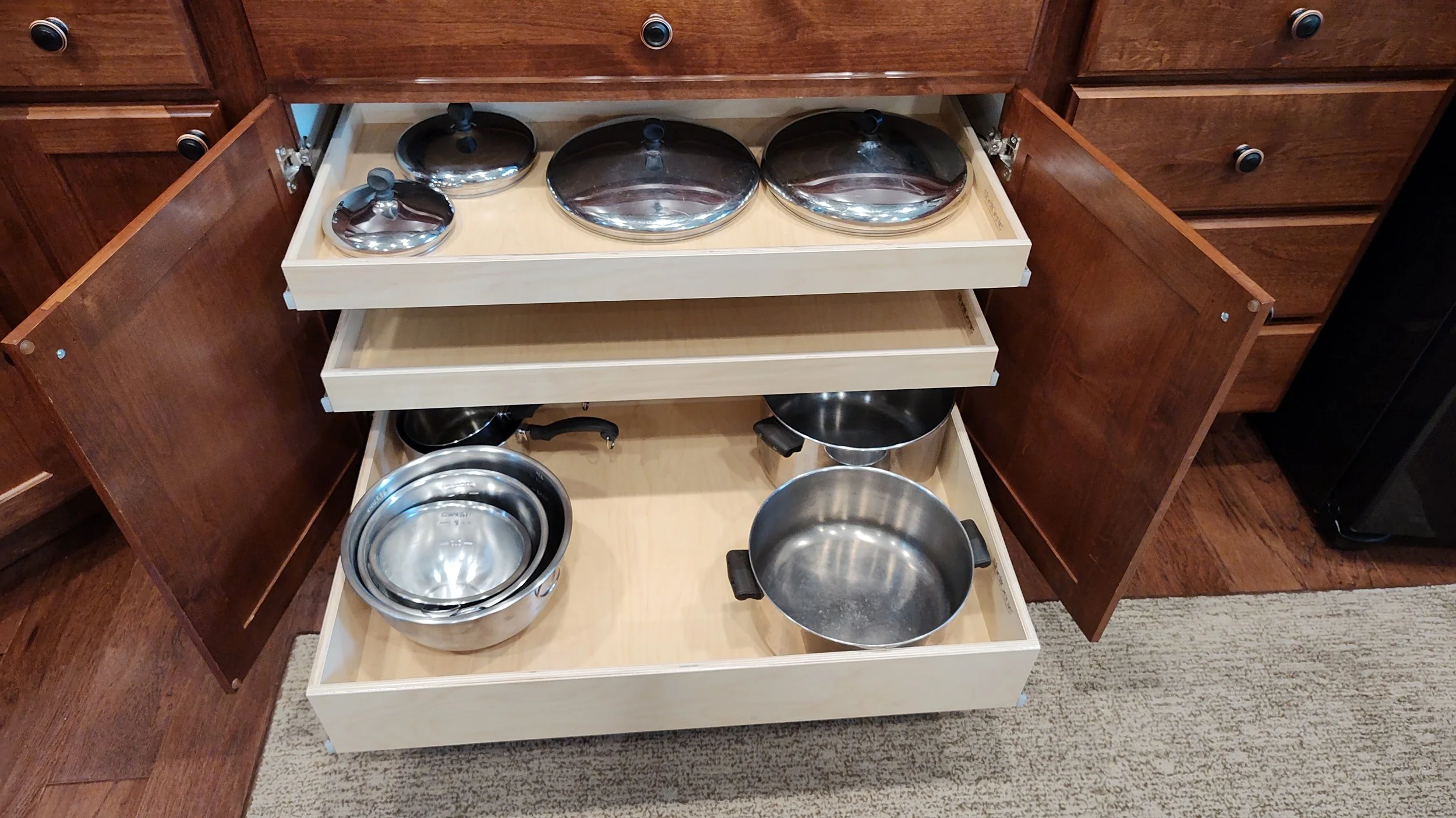 Open kitchen cabinet with wooden drawers containing stainless steel pots and pans.
