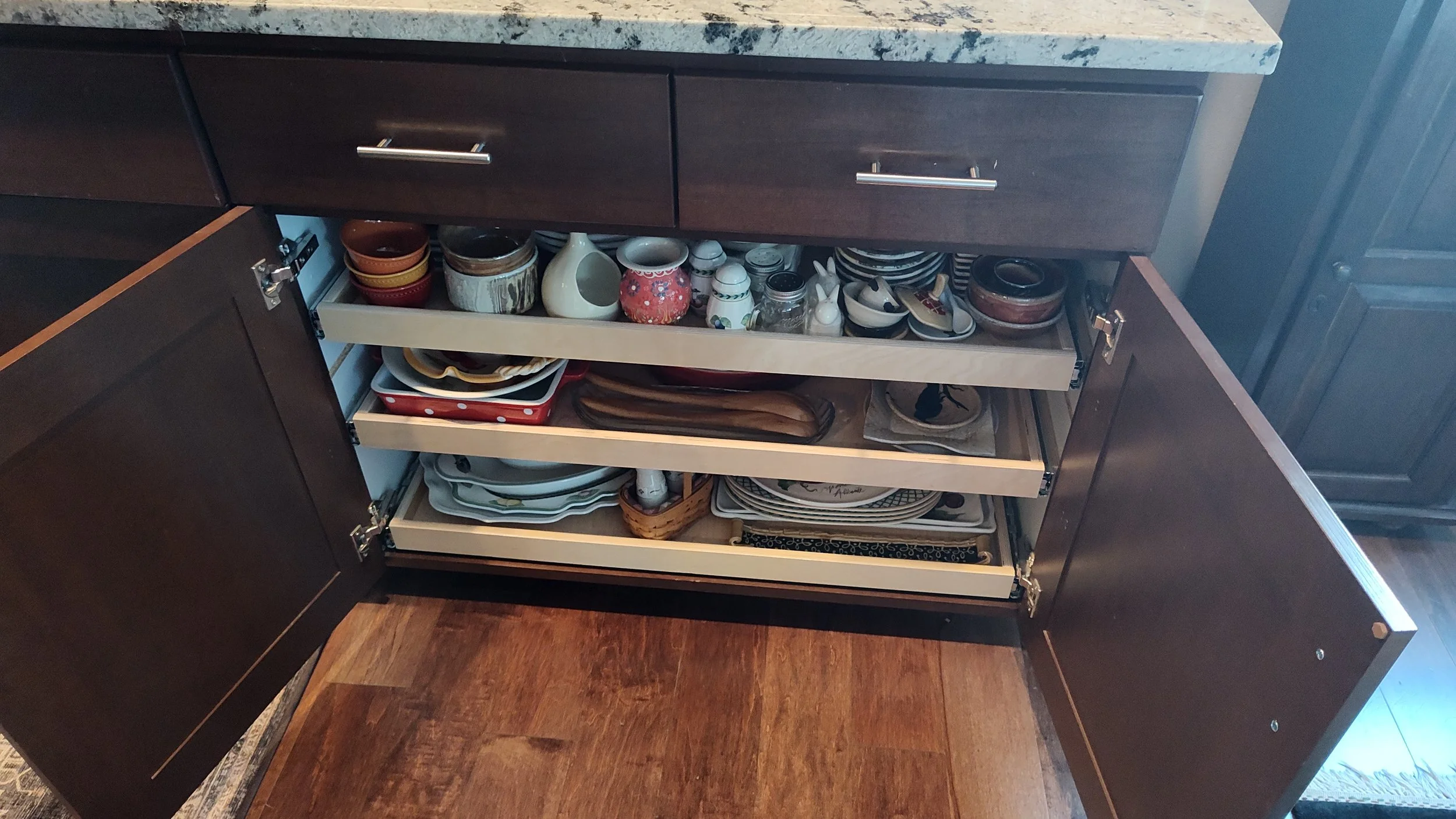Open kitchen cabinet with three shelves filled with bowls, plates, and small dishes on a kitchen countertop.