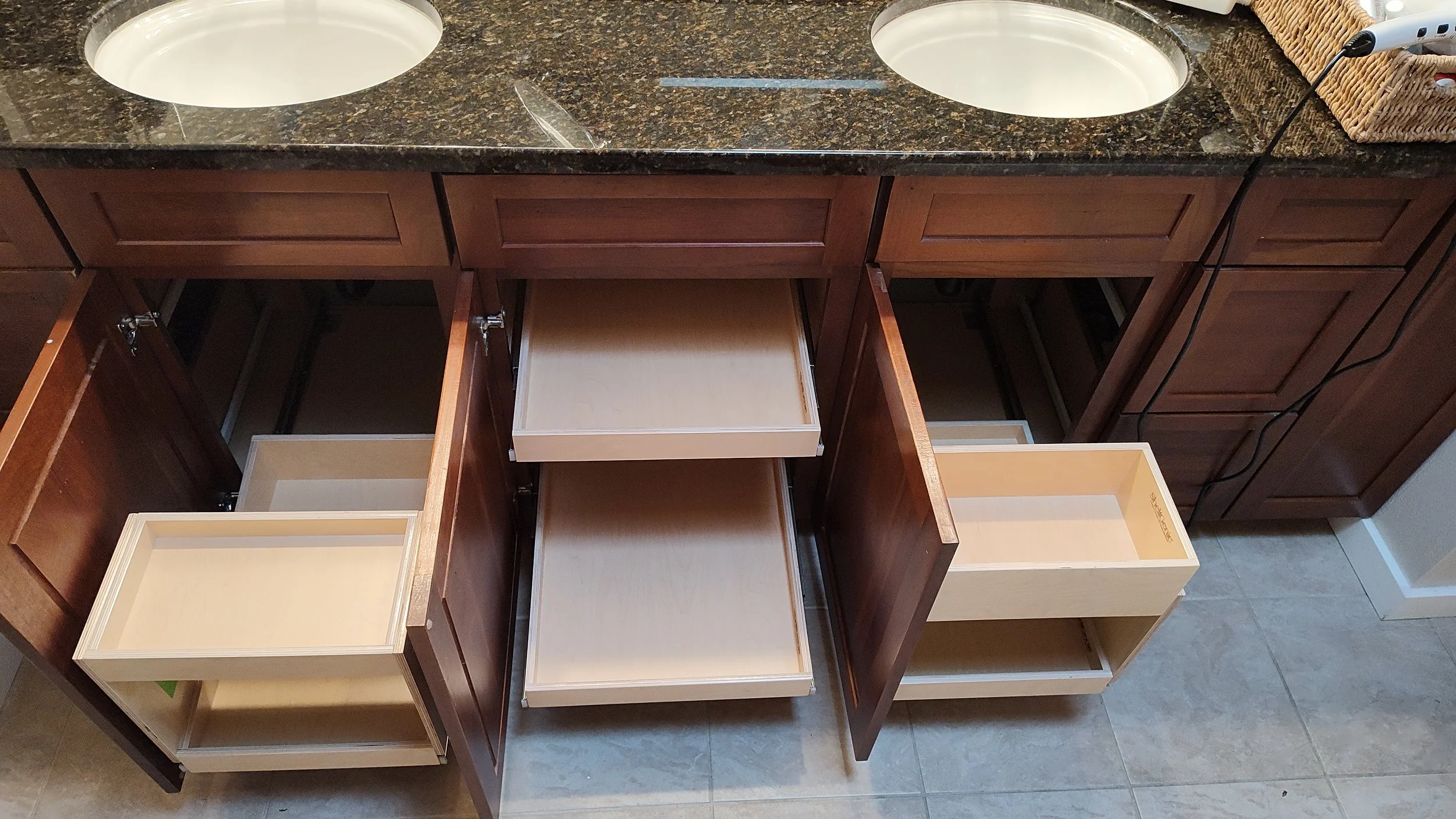 Open kitchen cabinet drawers and empty drawers with a granite countertop and sink with two basins