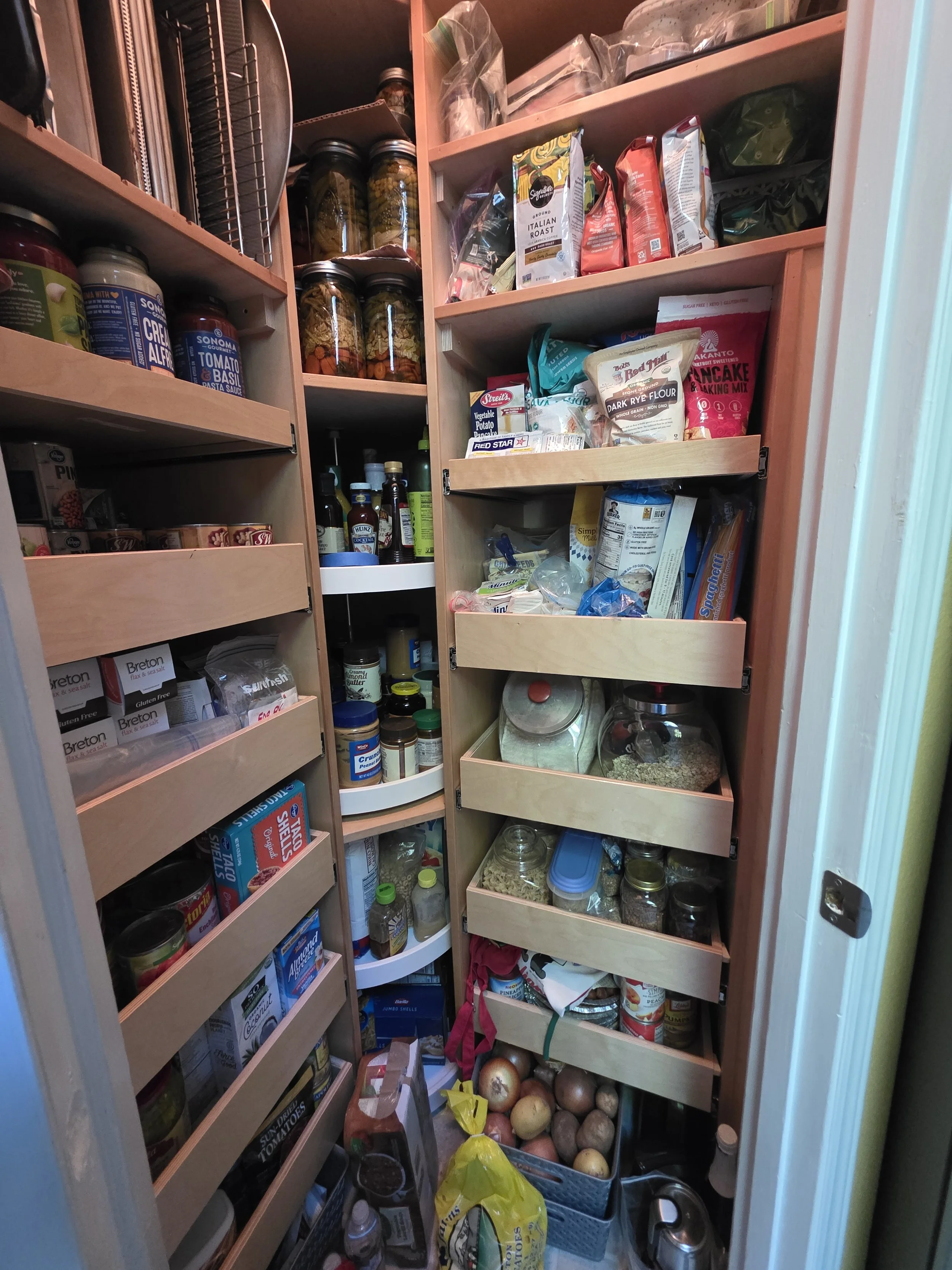 Pantry closet filled with jars, cans, boxed food, spices, and fresh onions on the floor.