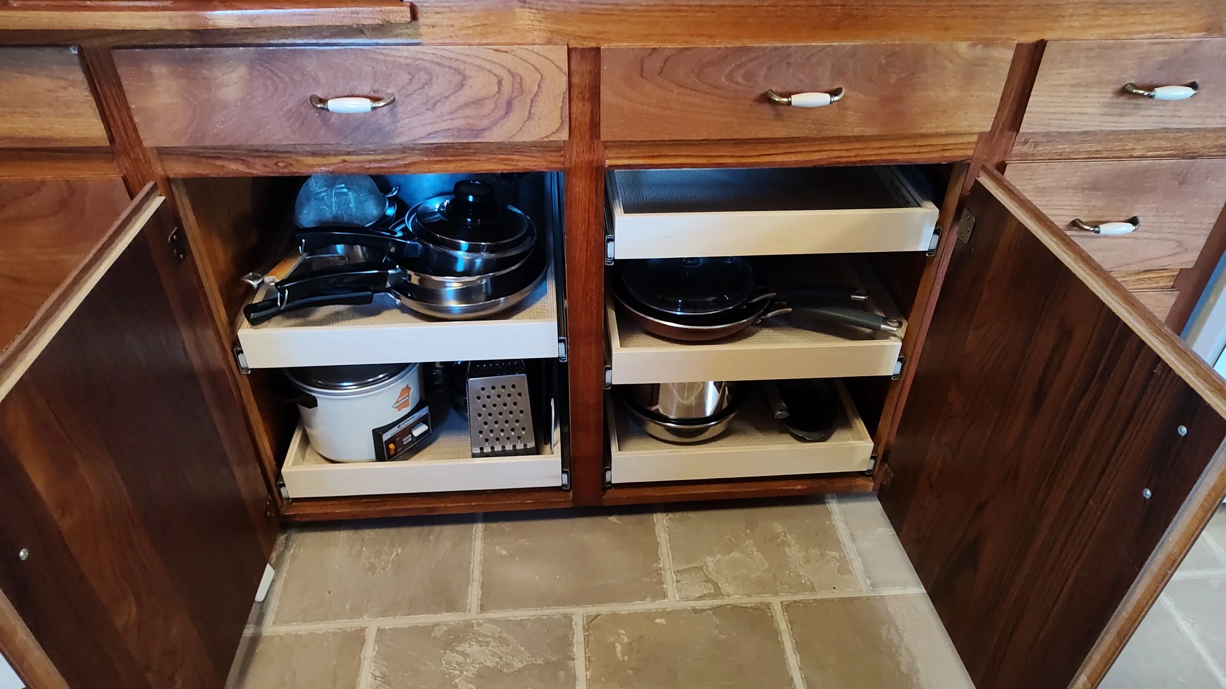 Open kitchen cabinet with pots, pans, and kitchen appliances on the shelves inside.