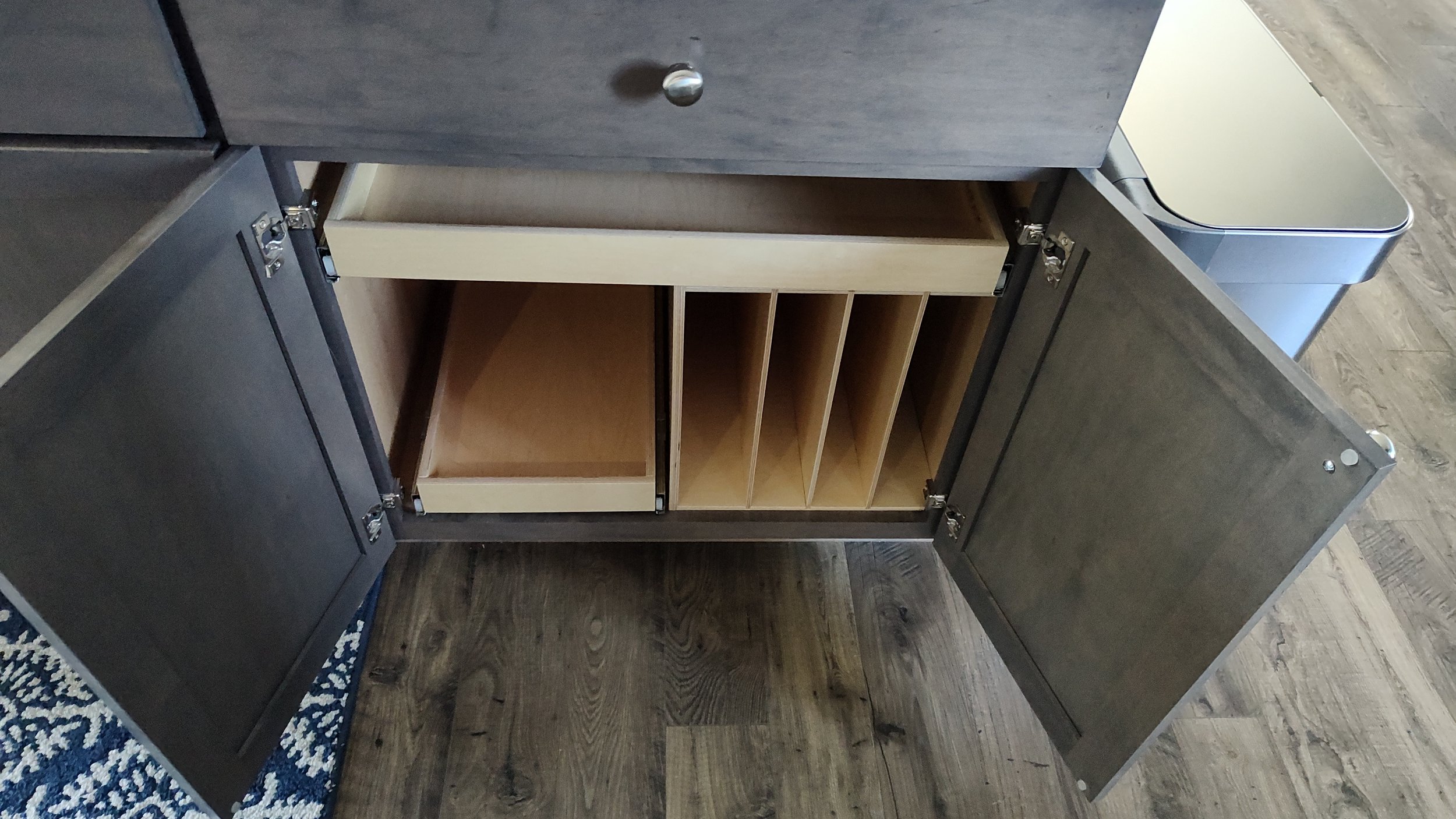 Open cabinet with multiple storage compartments, including pull-out drawers and cubbies, on a wooden floor.