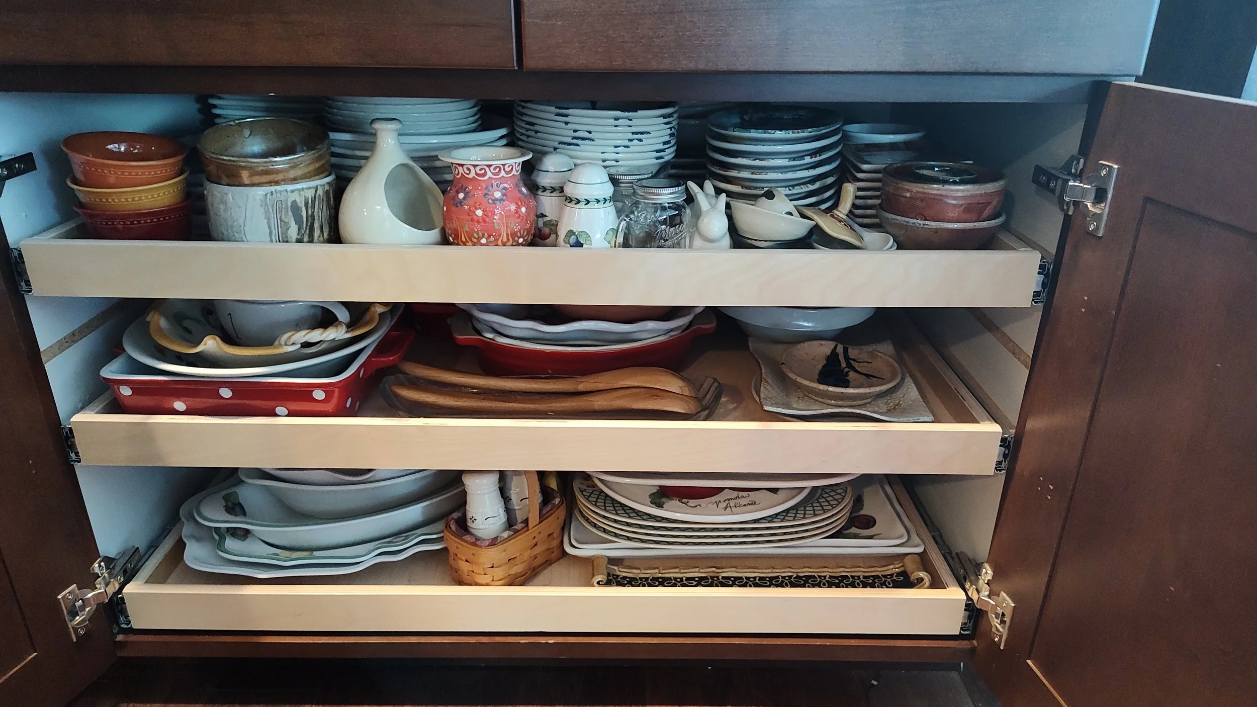 Kitchen cabinet with three open shelves filled with various dishes, bowls, cups, and decorative items.