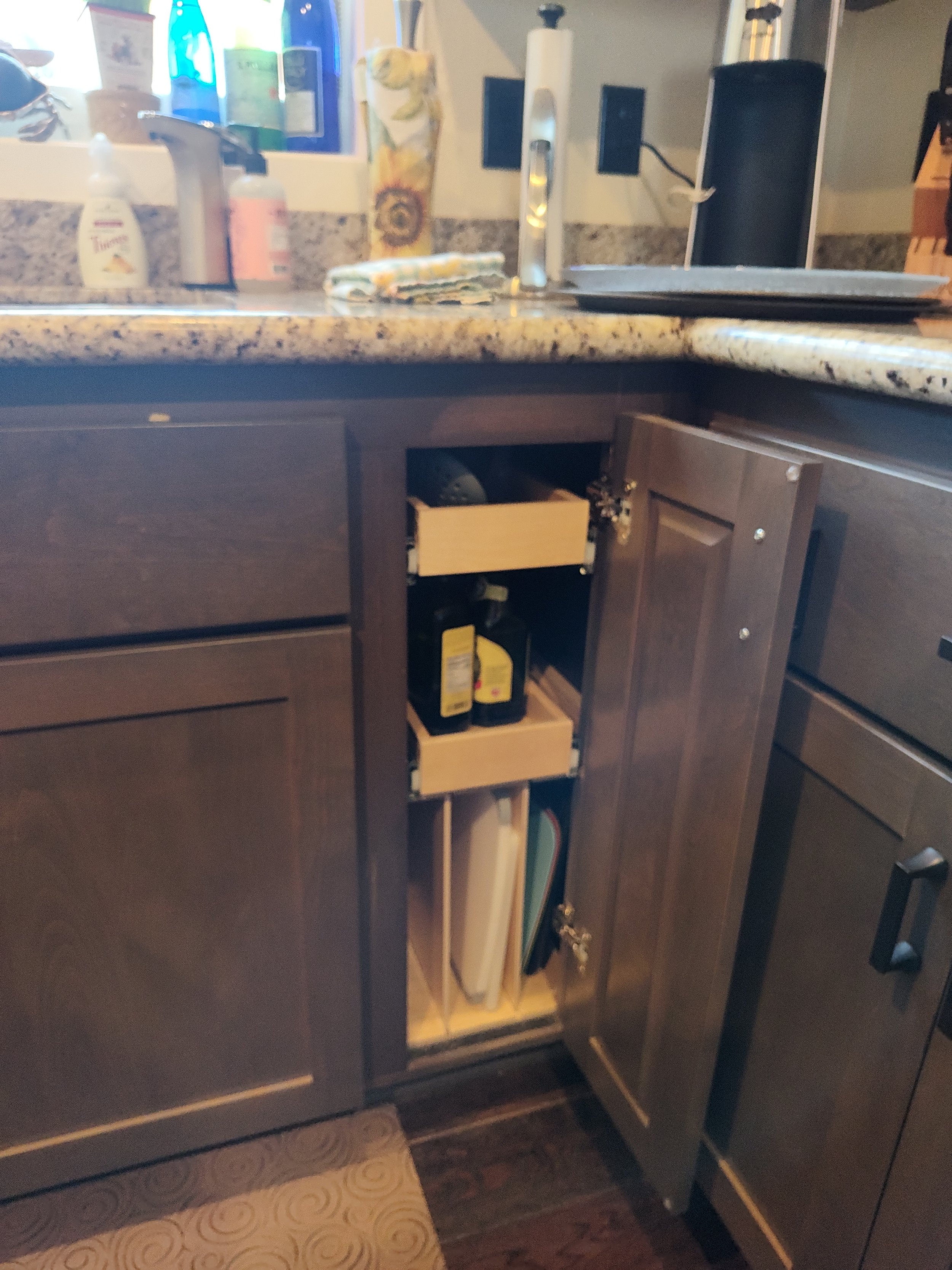 Open cabinet under kitchen counter with spice bottles, cutting boards, and various kitchen items visible.