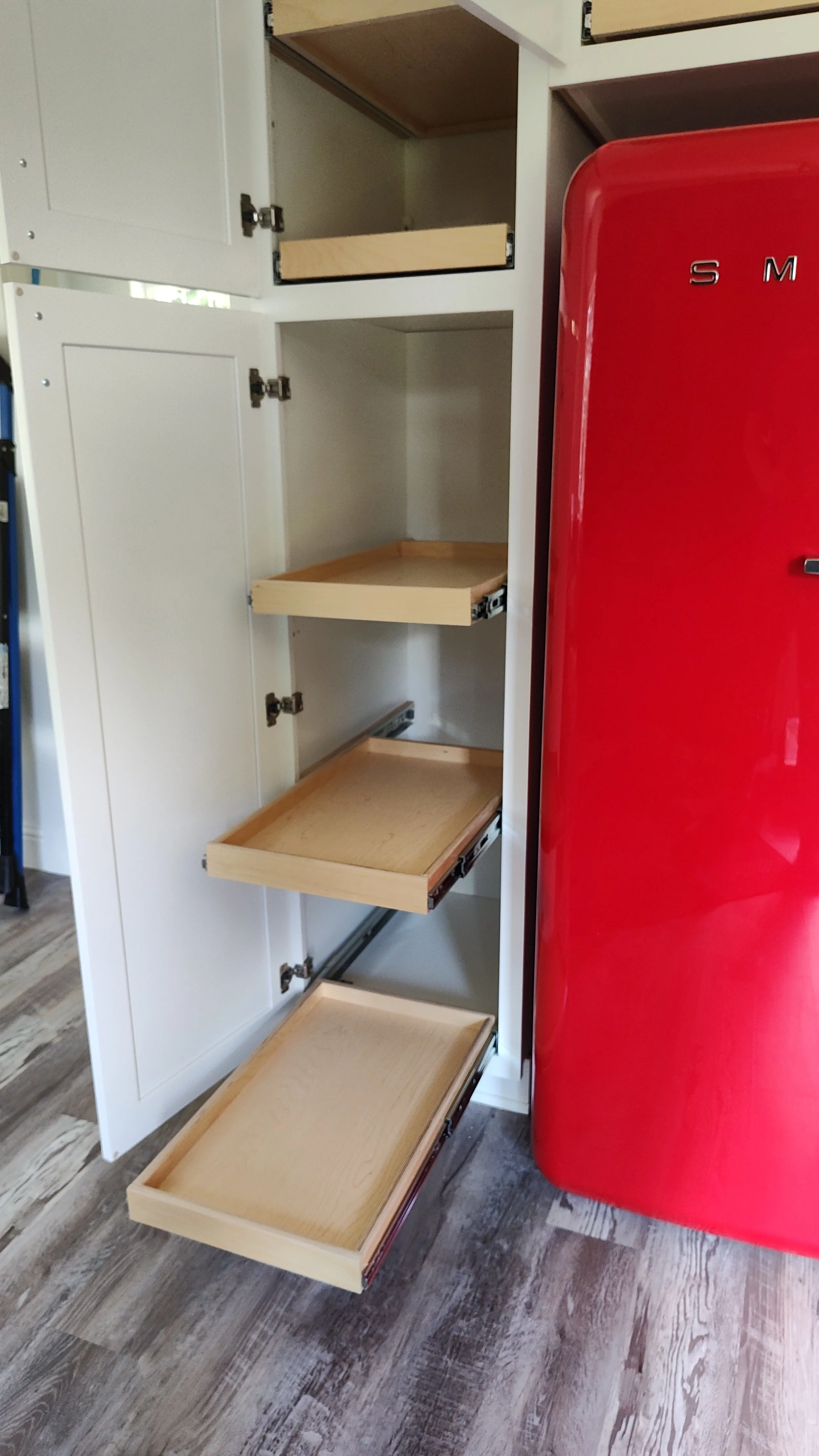 White kitchen cabinet with open drawers and a red vintage refrigerator beside it. The drawers are partially pulled out, revealing their wooden interiors.