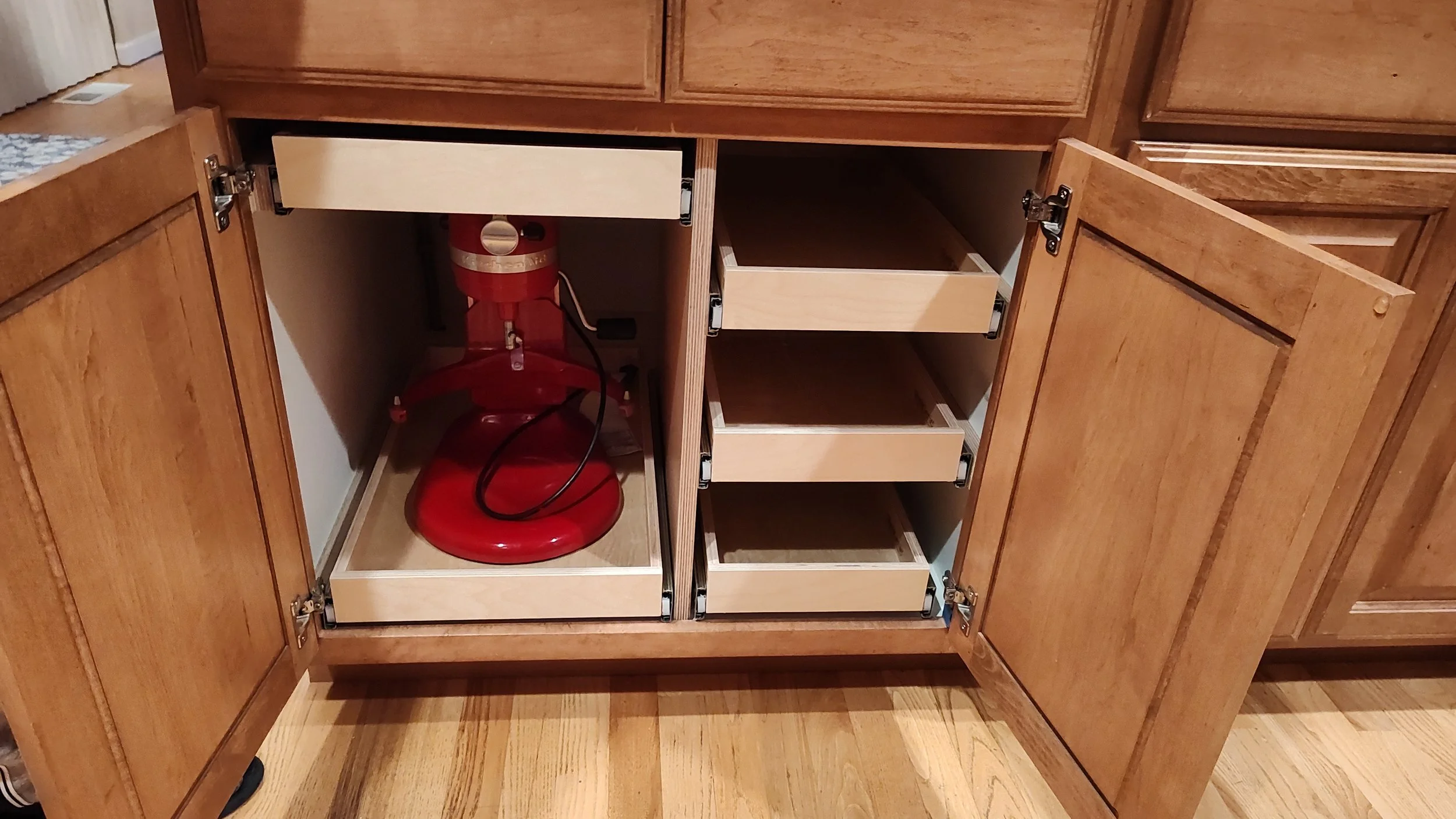 An open kitchen cabinet with a red vintage-style fire extinguisher inside, and empty pull-out drawers.