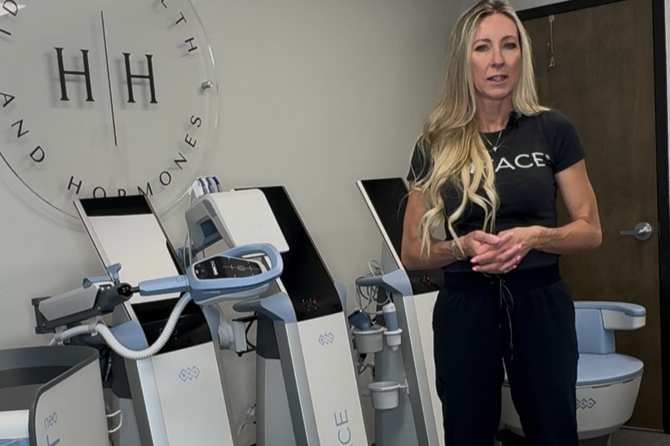 Six women sitting on a ledge by the ocean with their arms raised during sunset.