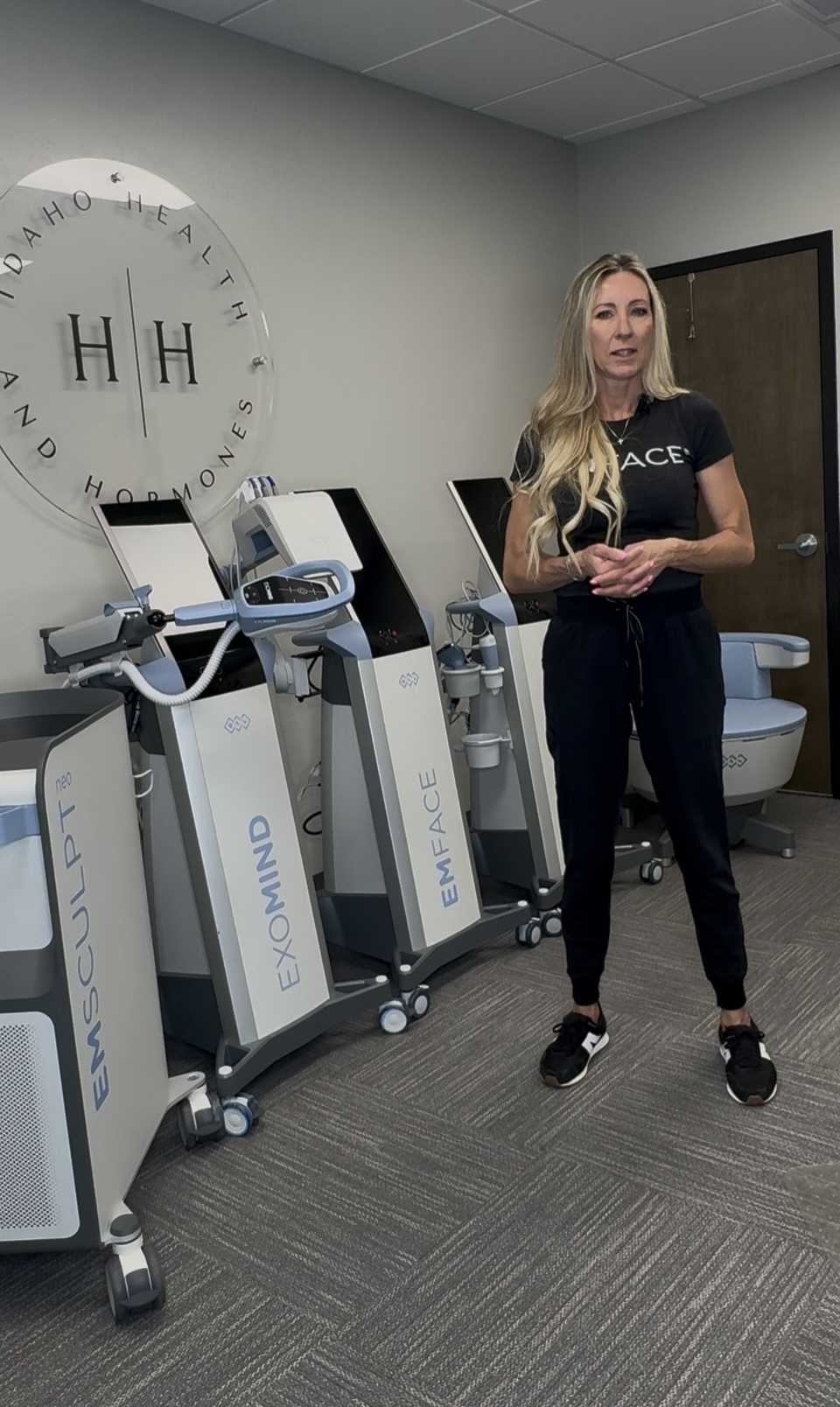 Six women sitting on a ledge by the ocean with their arms raised during sunset.
