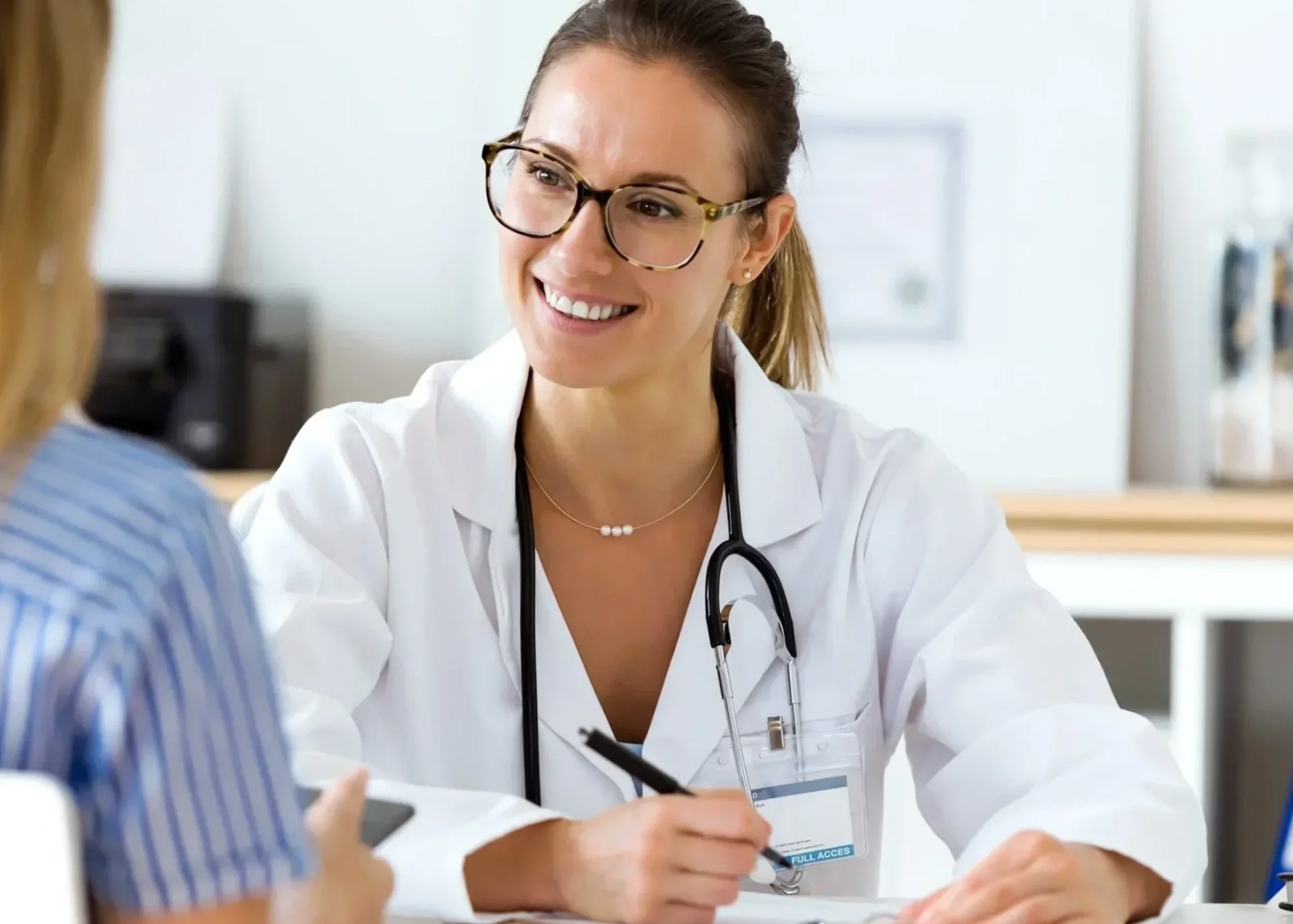 A smiling woman is on a man's back, both are outdoors on a bridge. The woman has dark hair and the man has a beard and short hair. They are happy and enjoying the moment.