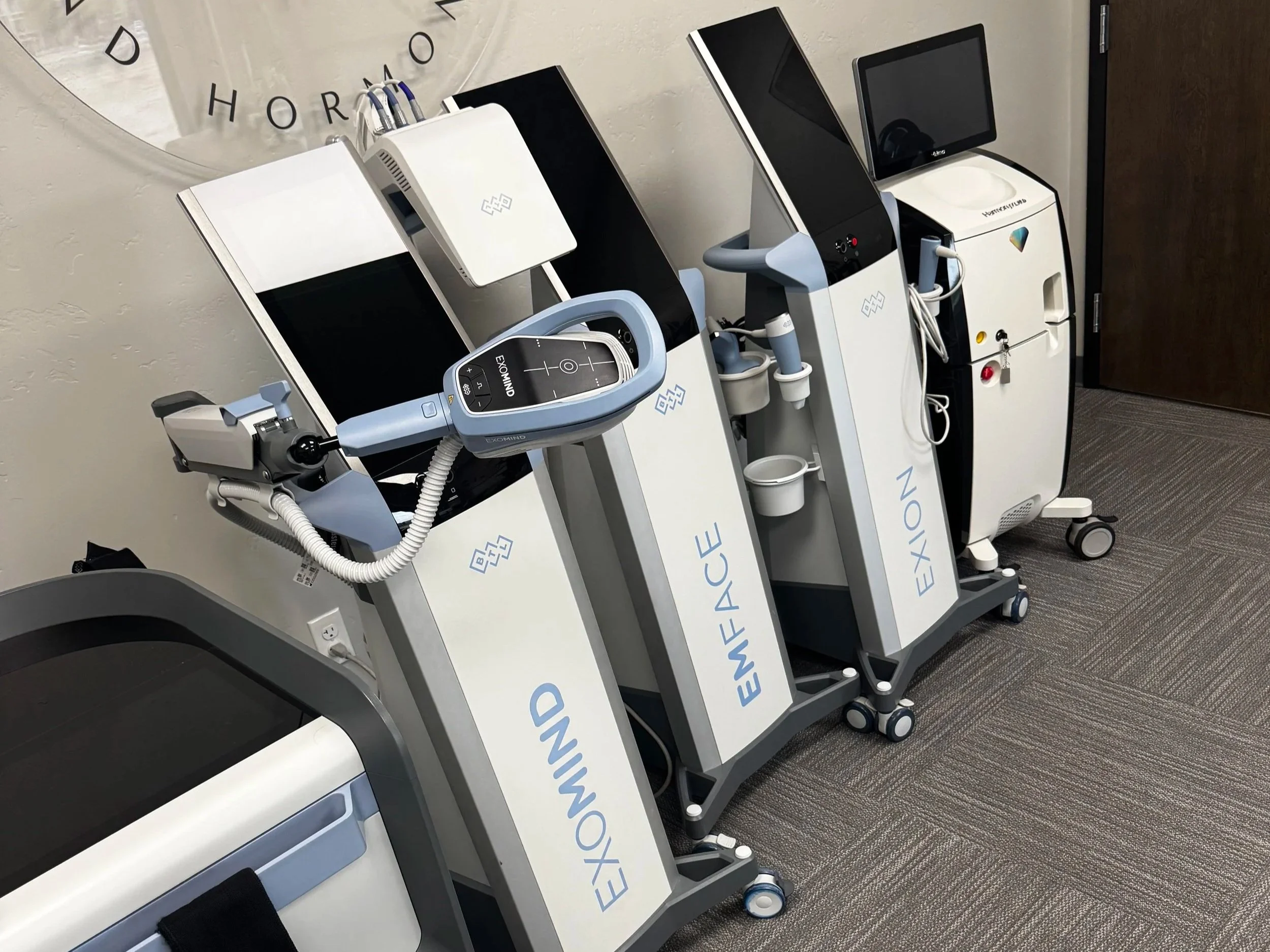 Six women sitting on a ledge by the ocean with their arms raised during sunset.