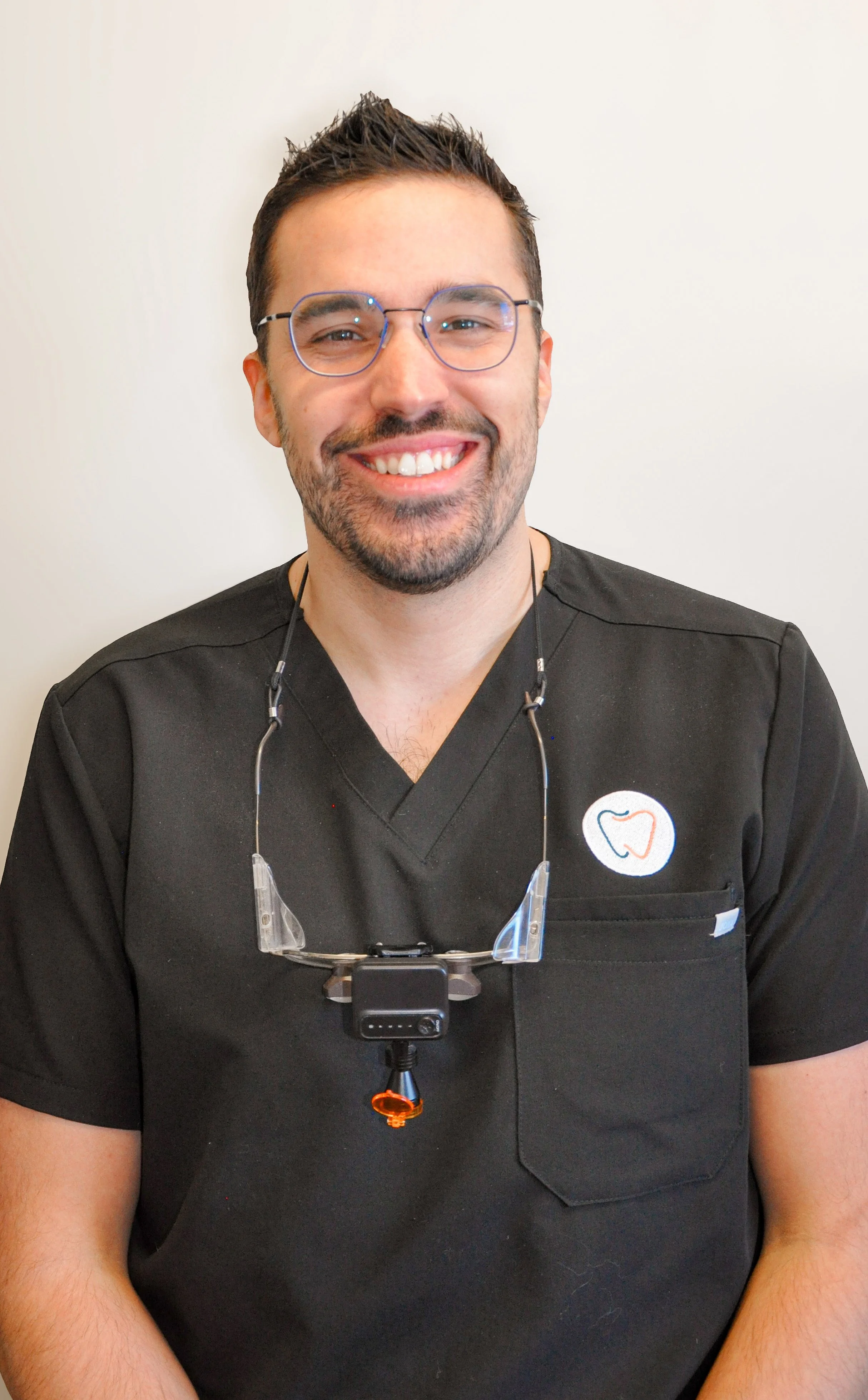 Dentiste homme souriant en uniforme professionnel avec lunettes de loupe, soins dentaires modernes et expertise.
