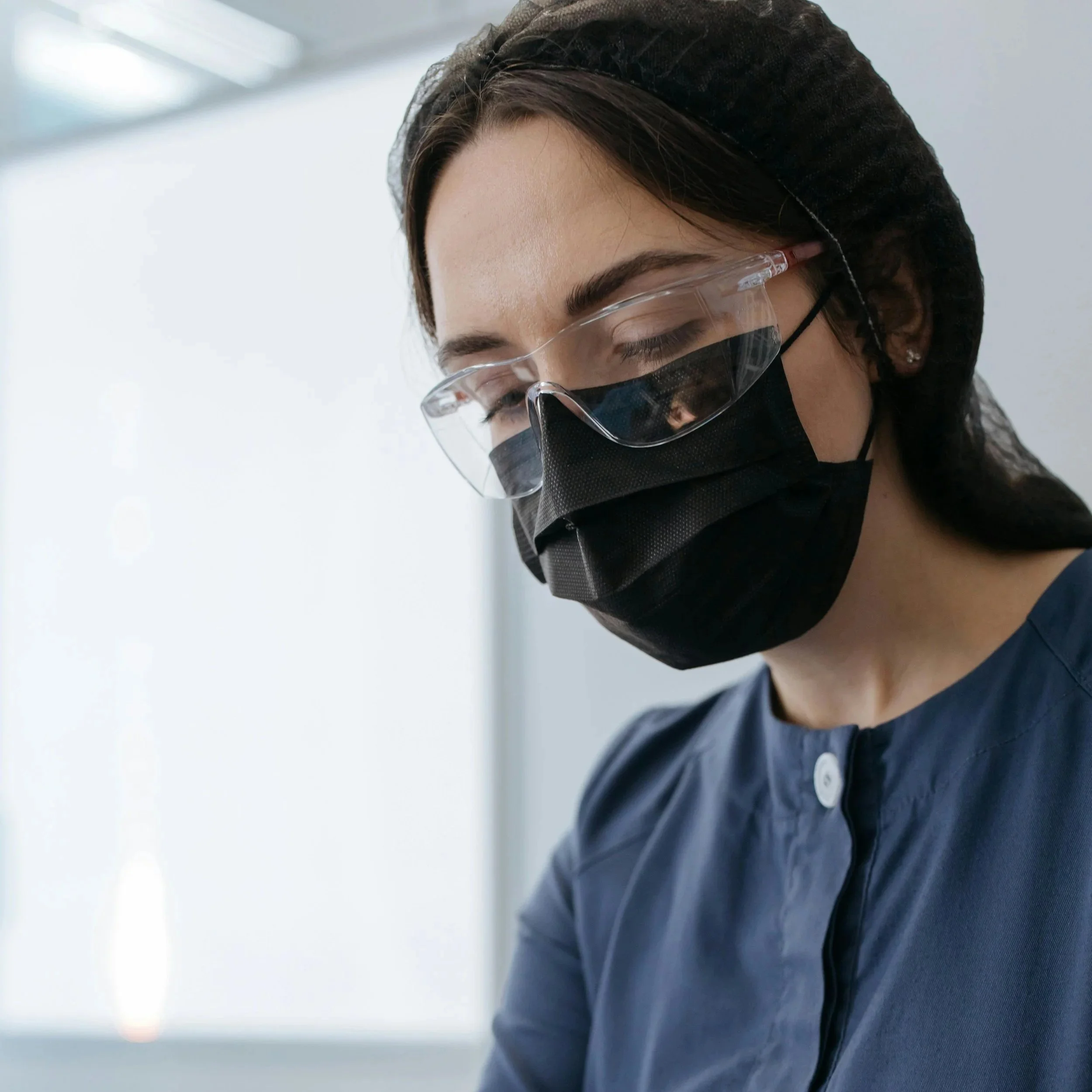 Une jeune femme aux cheveux bruns foncé, portant un masque chirurgical regarde son patient.