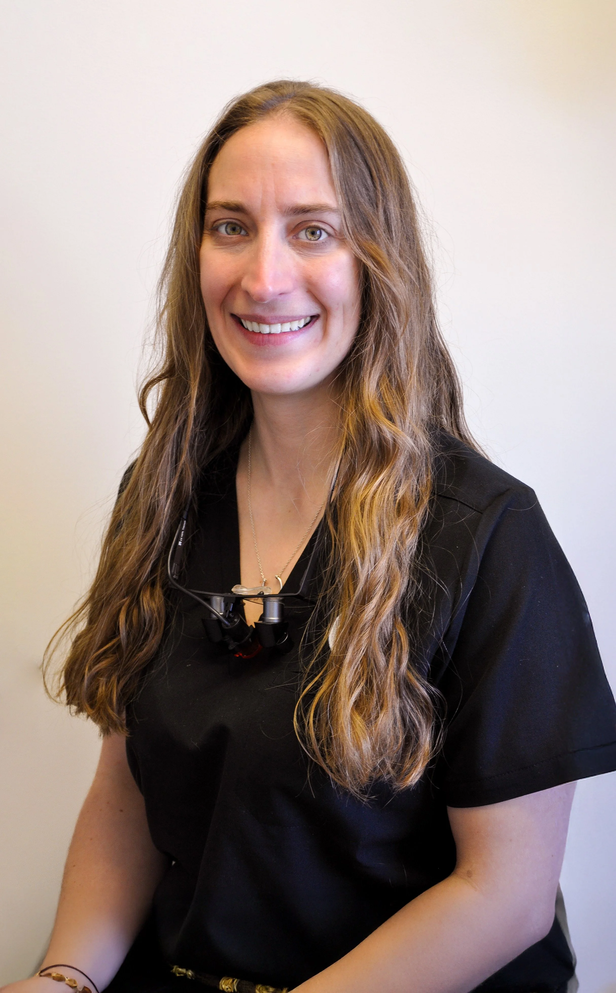 Dentiste femme souriante en uniforme professionnel avec lunettes de loupe, soins dentaires modernes et expertise.