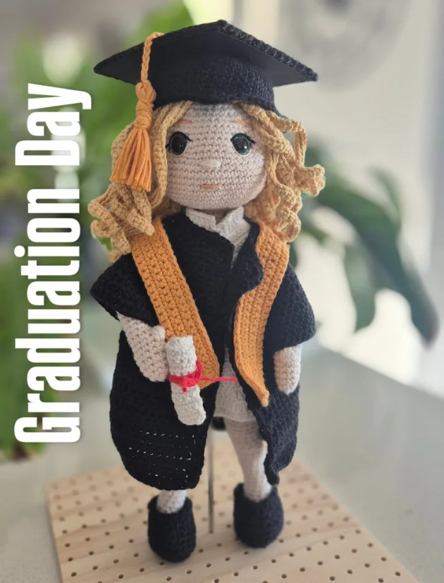 Crocheted doll dressed in cap and gown holding a diploma for graduation day.