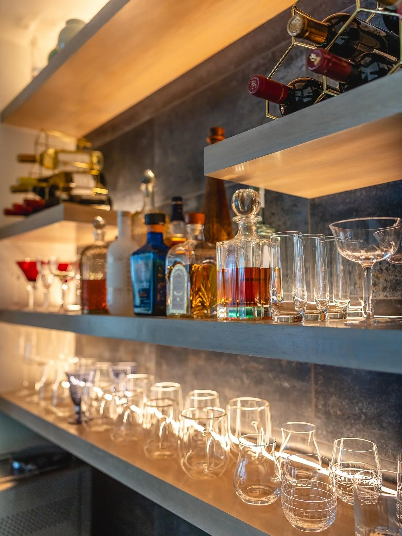 We create a custom combination coffee and wine bar in just about every project and this is one of our favorites. New and vintage glassware sparkles with the dimmable uplighting we integrated into the top of each shelf. The amazing tile from @walkerza