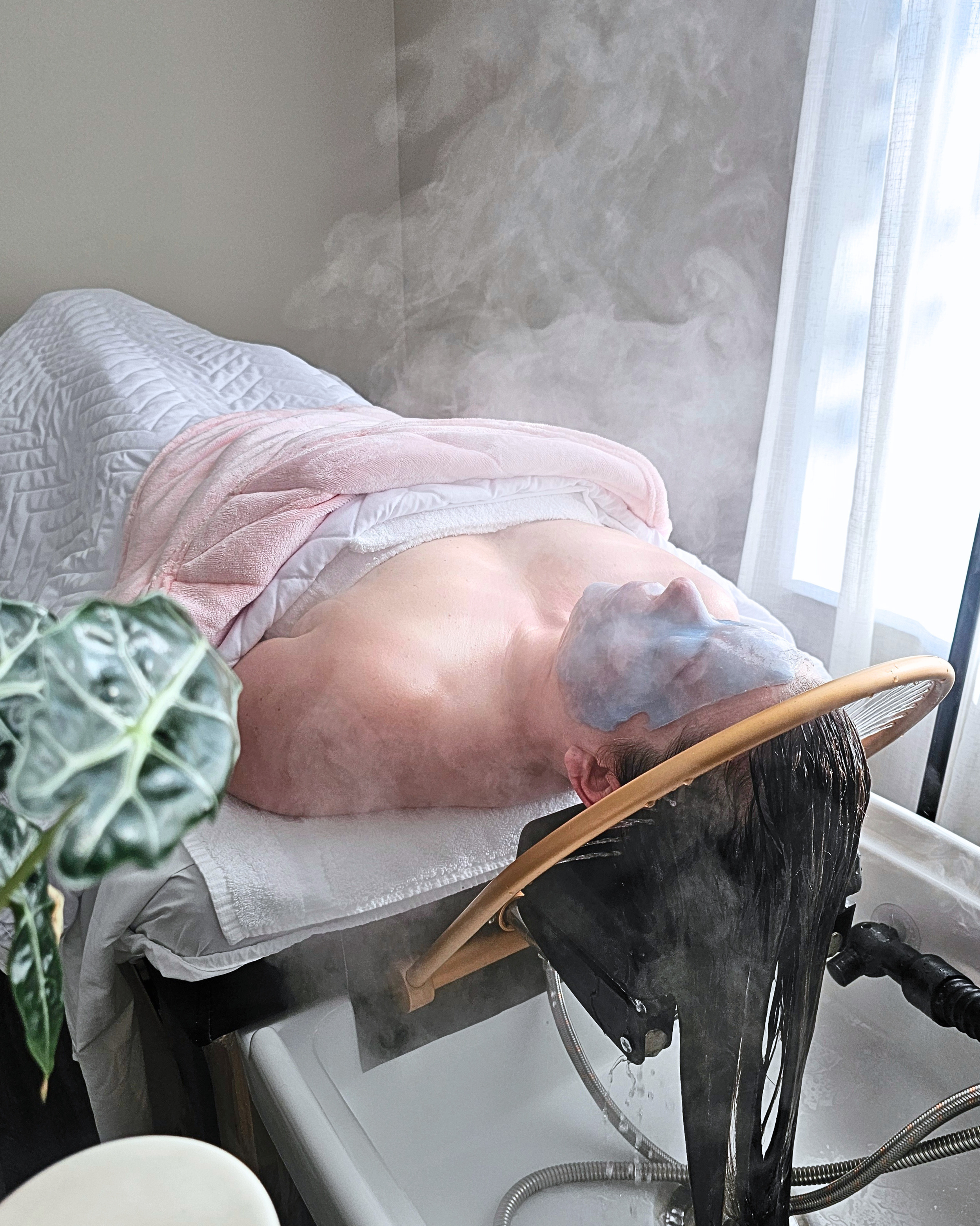 A person laying on a head spa bed, enveloped by steam.