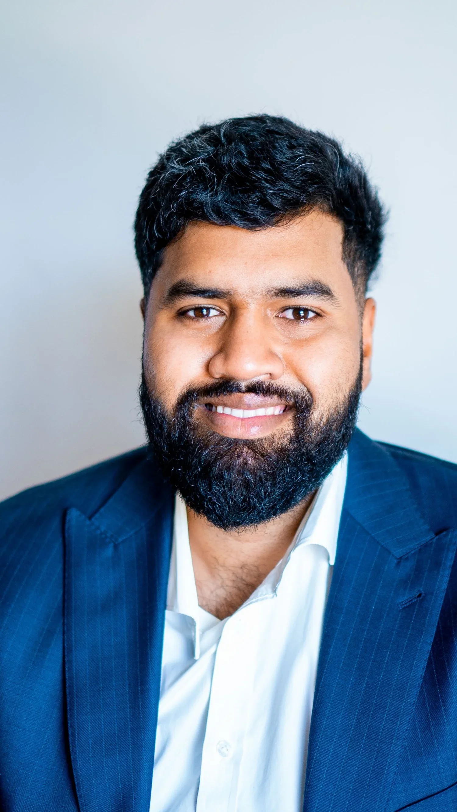 A professional man smiling in a suit and white shirt against a plain light background.