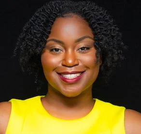 A smiling woman with curly black hair wearing a yellow top against a black background.