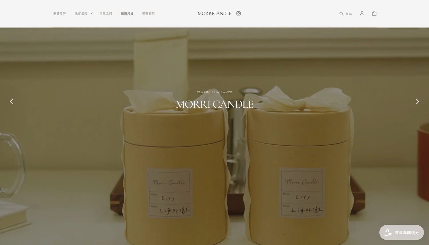 Two beige candles in round containers with white tissue paper tied on top, placed on a white surface. Labels on the candles read 'MORRI Candle' and 'City' with some text in Chinese.