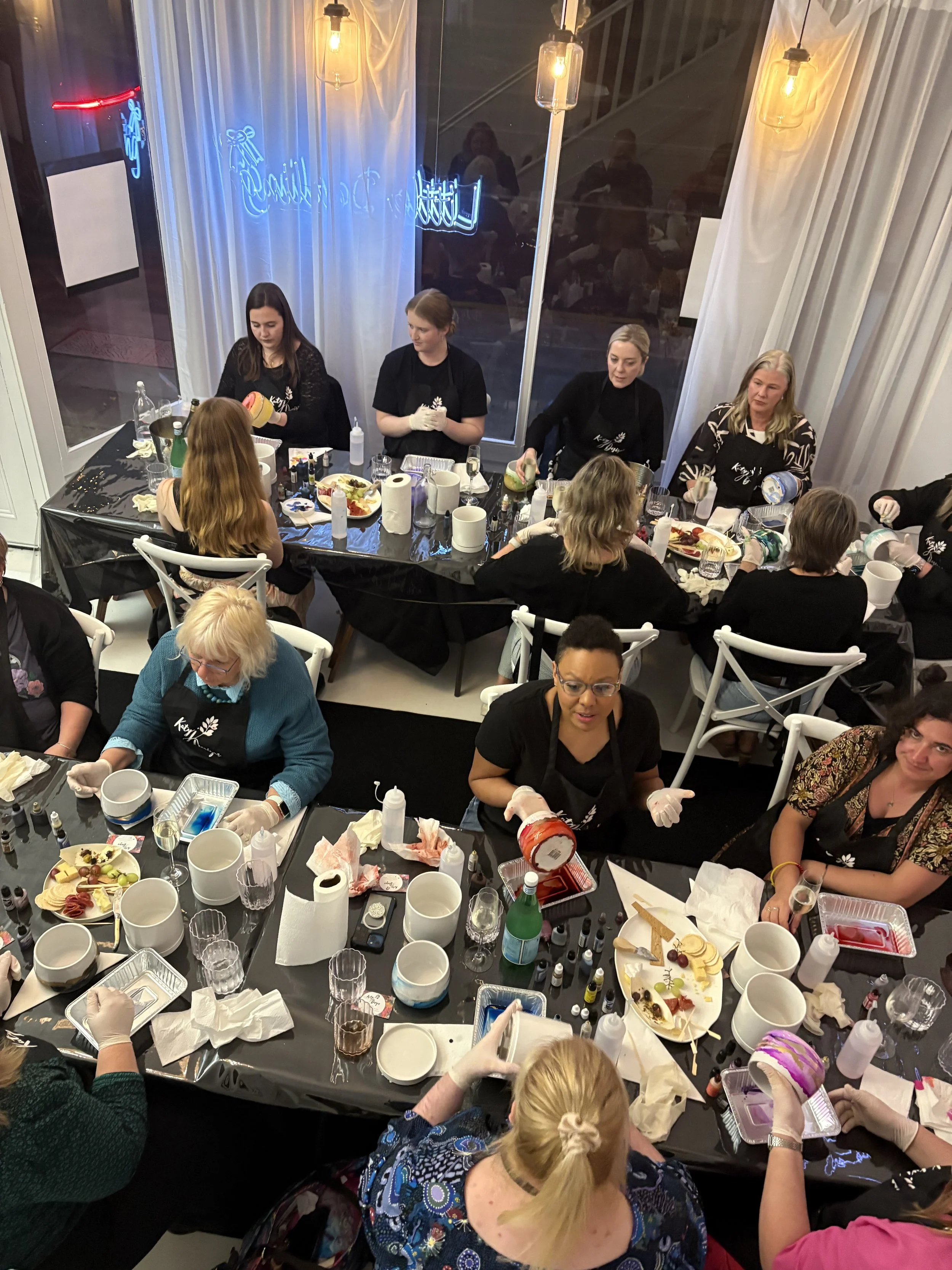 Group of women decorating cakes at a cake decorating class or workshop, with supplies and ingredients on the tables.
