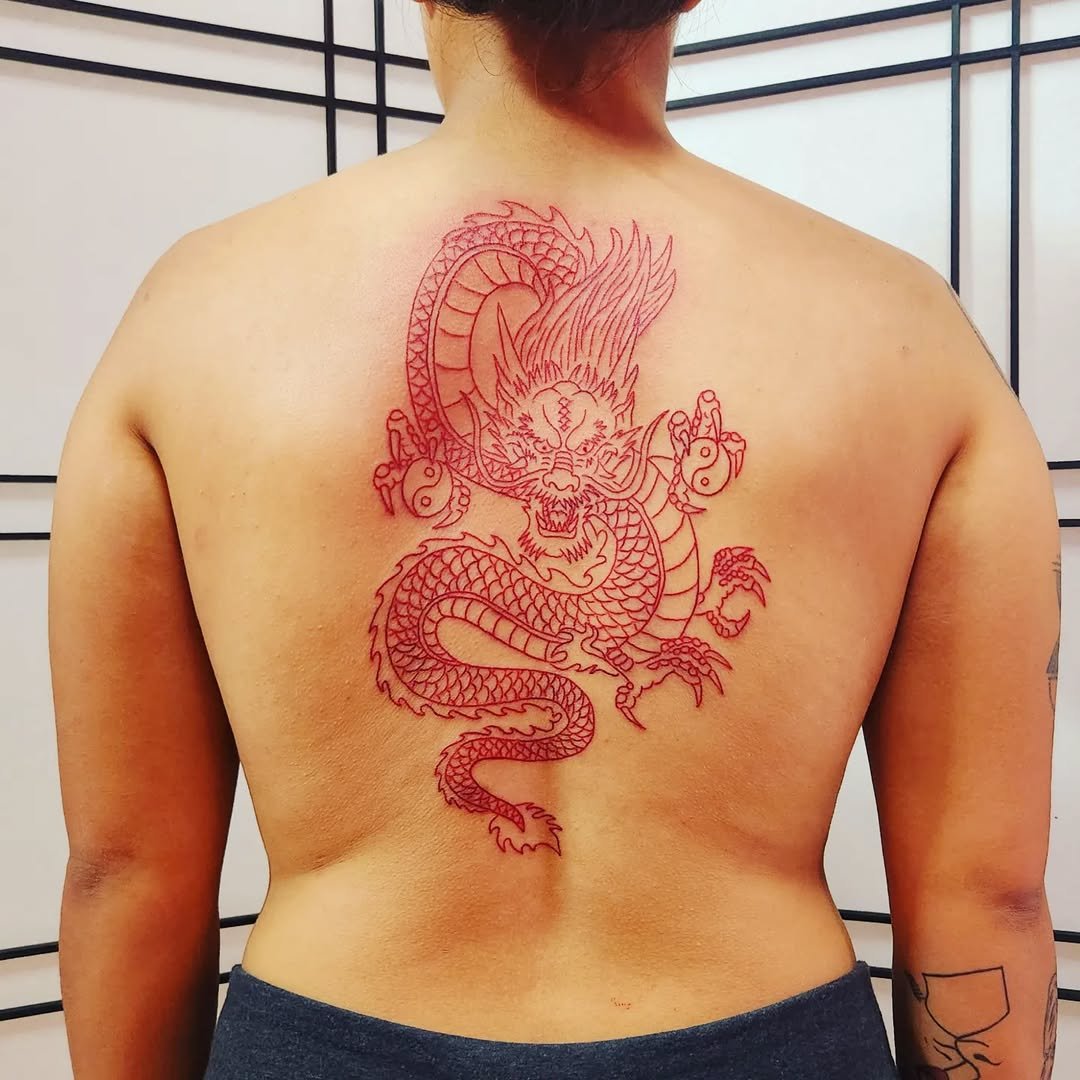 Red outline tattoo of a dragon on a person's back with tribal elements and a fierce face.