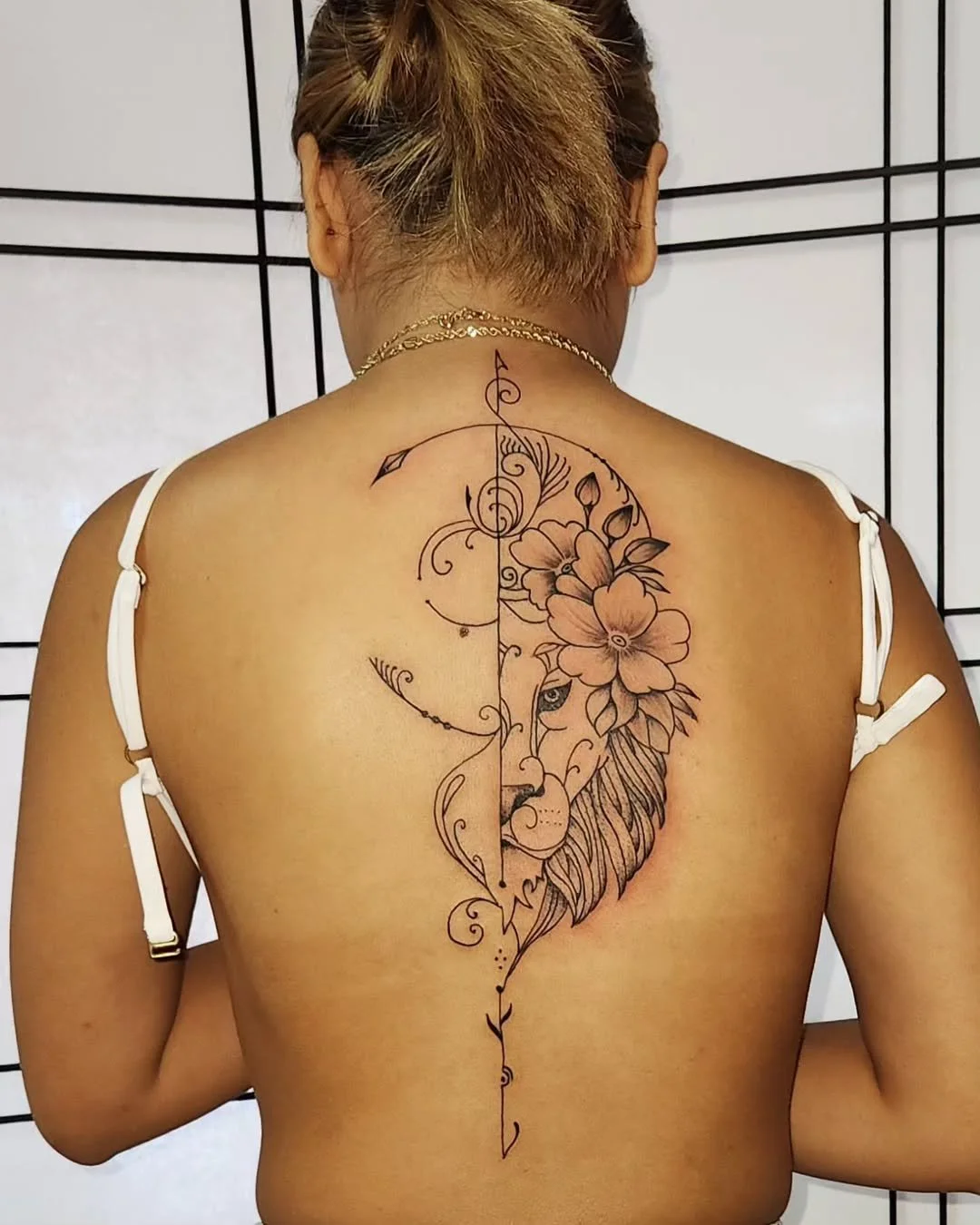Back of a woman with a large tattoo of a lion and flowers, divided by a vertical line.
