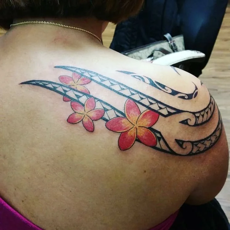 Tattoo of pink and yellow cherry blossoms with black tribal-style design on shoulder.