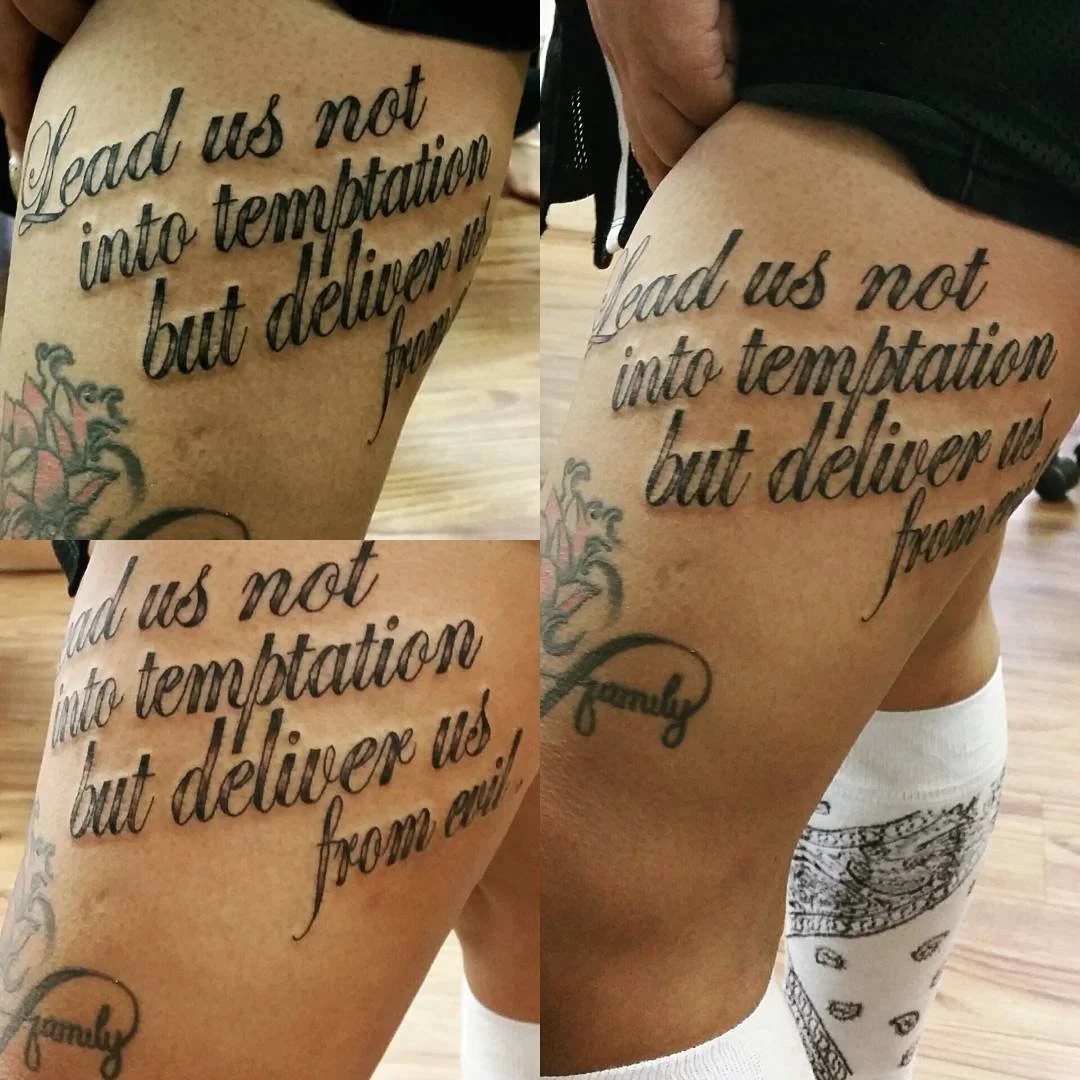 Tattoo on a person's thigh with the text, "Lead us not into temptation but deliver us from evil," and a small floral design with the word "family" written below.