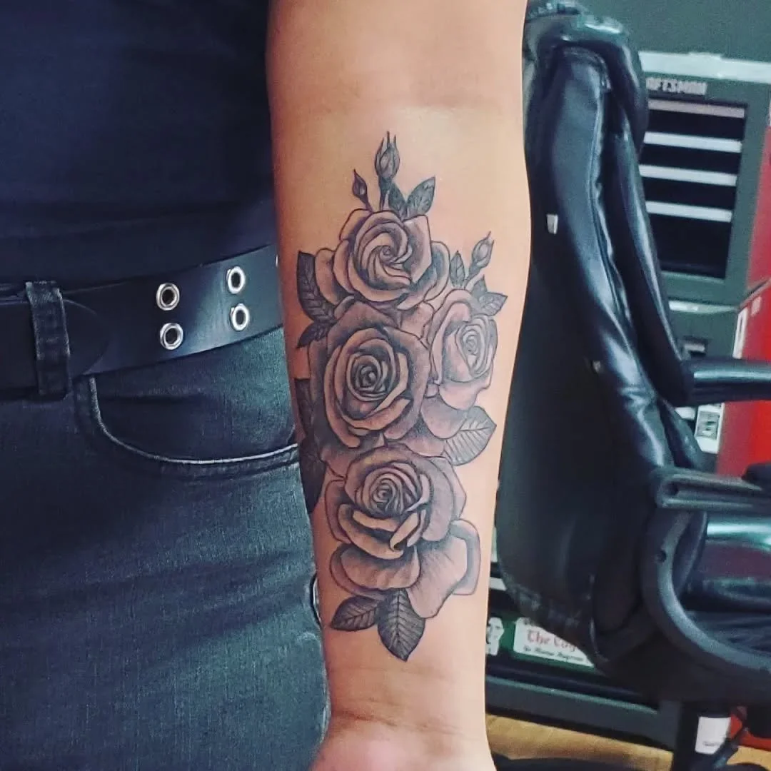 Black and gray tattoo of five roses with leaves on a person's forearm.