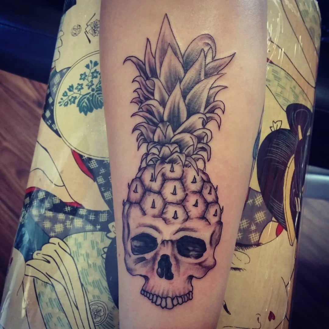Tattoo of a skull with a pineapple crown on the arm.