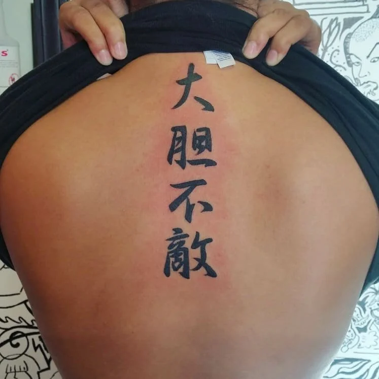 Tattoo of Chinese characters on lower back, with person lifting shirt to reveal tattoo.