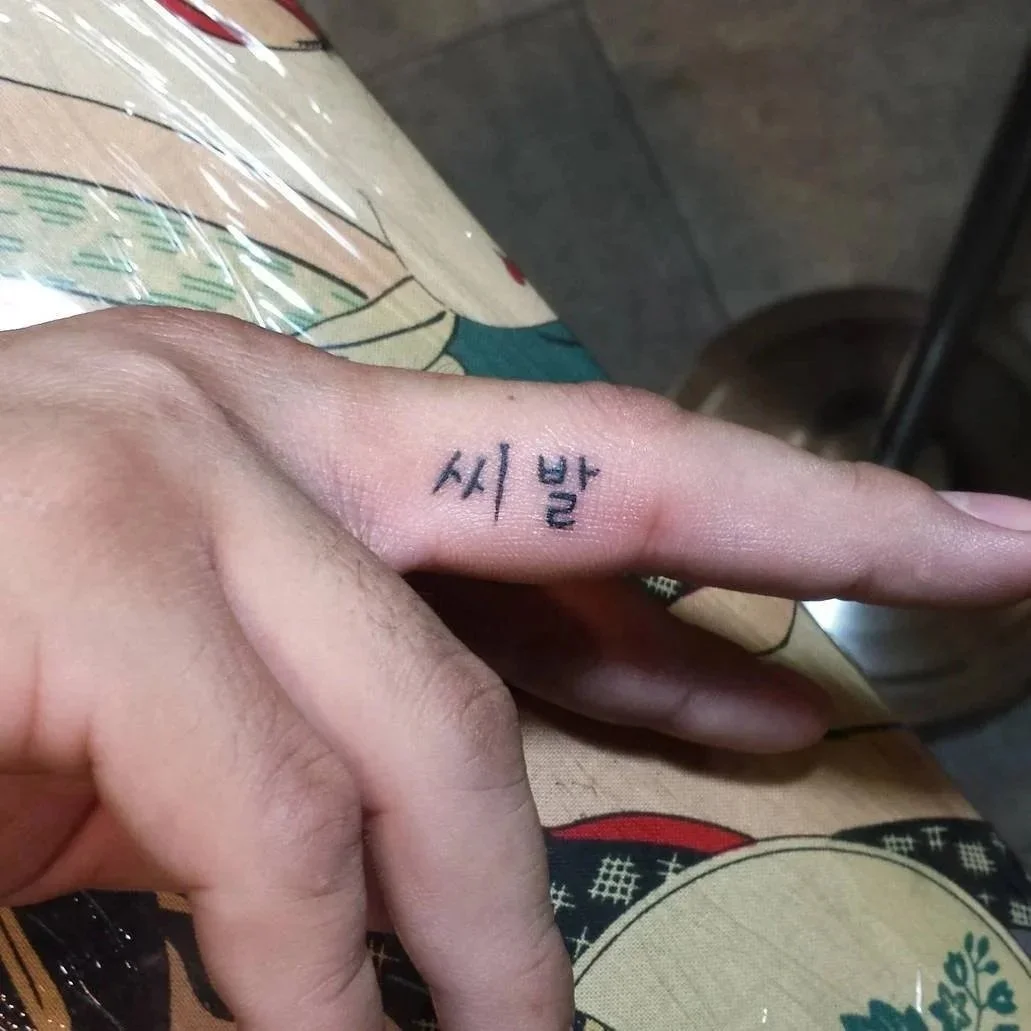 A person's hand with a small tattoo of Korean characters on their finger.