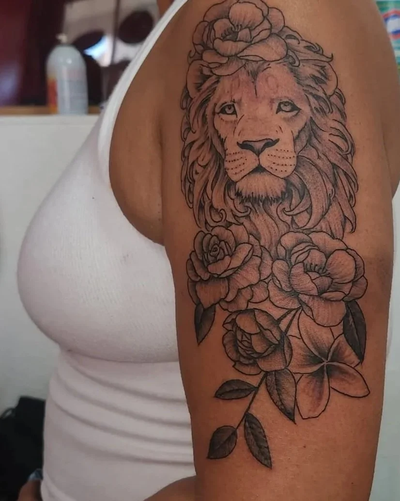 Tattoo of a lion's face with a floral crown and roses on the arm.